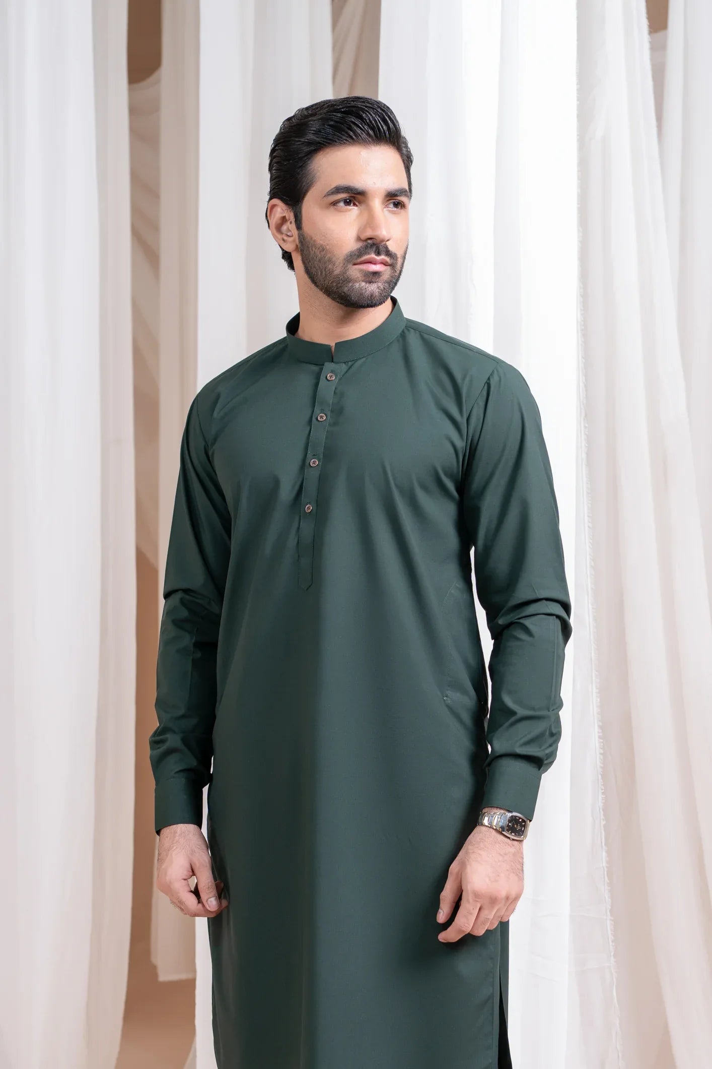 A man wearing a luxury blended kurta shalwar in green color with a mandarin collar and full sleeves. The outfit includes a patch pocket waistcoat.