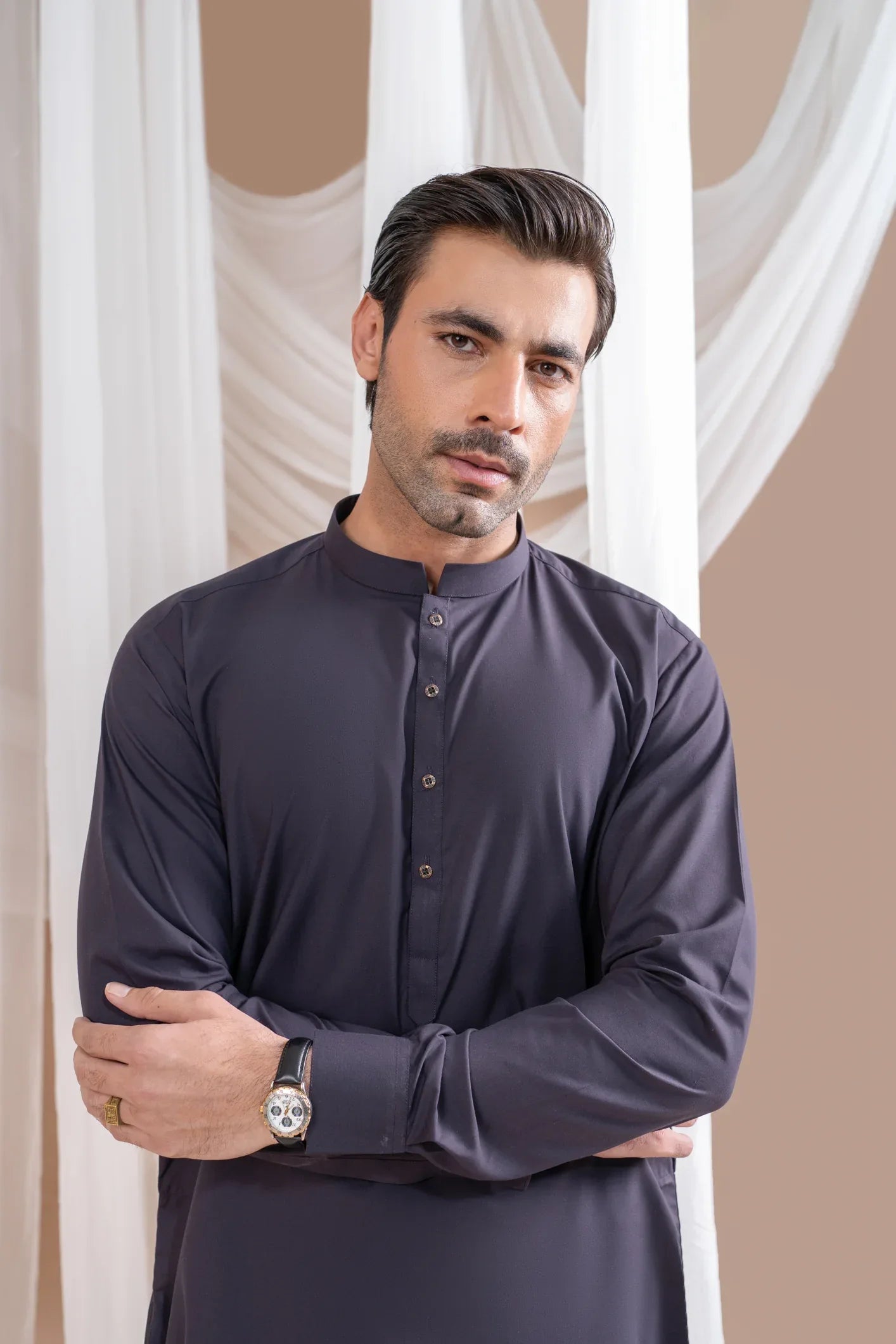A man wearing a deep burgundy luxury blended kurta shalwar and waistcoat, standing in a room with white drapes in the background.