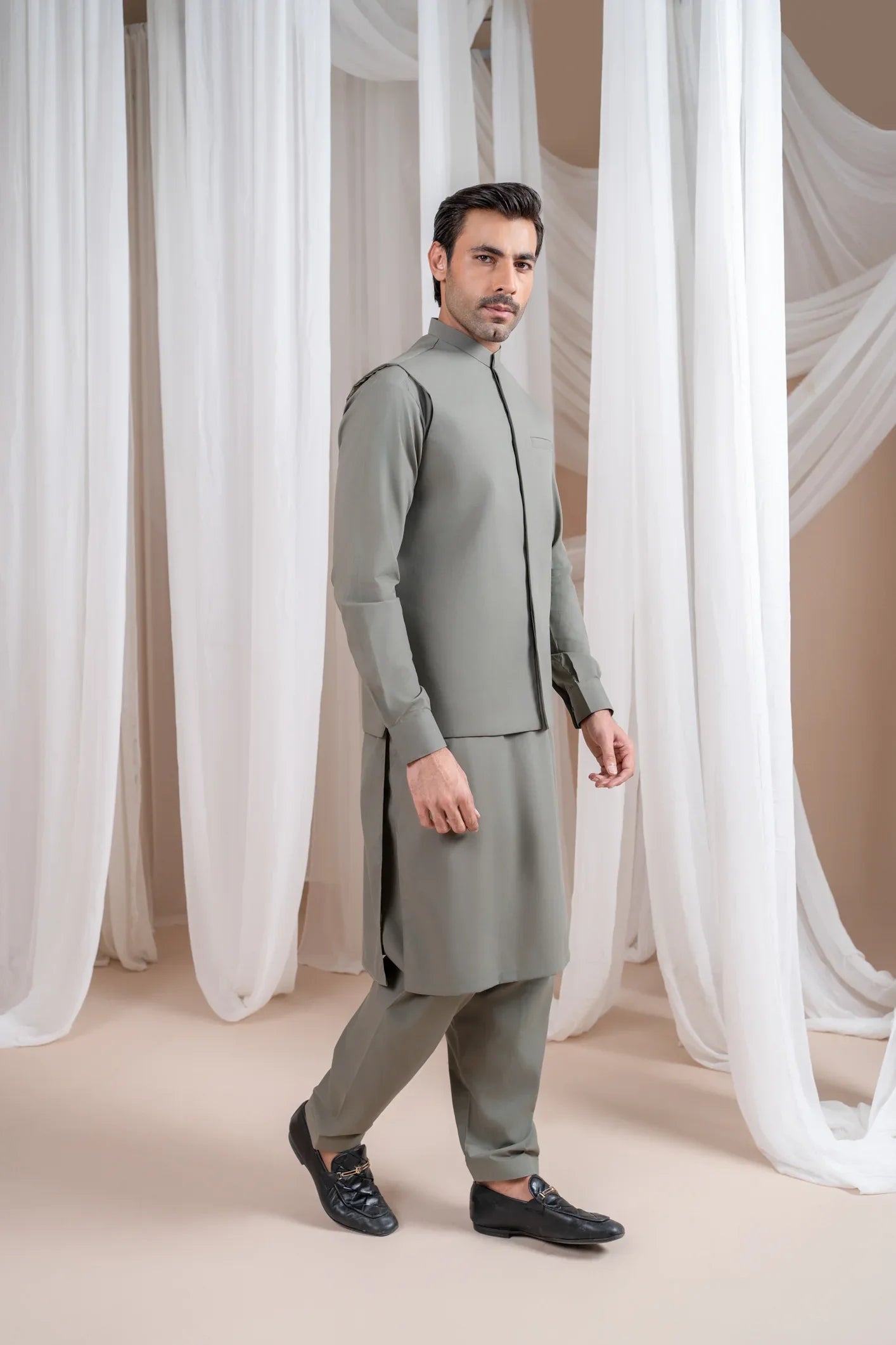 A man wearing a sand grey luxury formal Kameez Shalwar with a straight cut waistcoat and a patch pocket waistcoat.