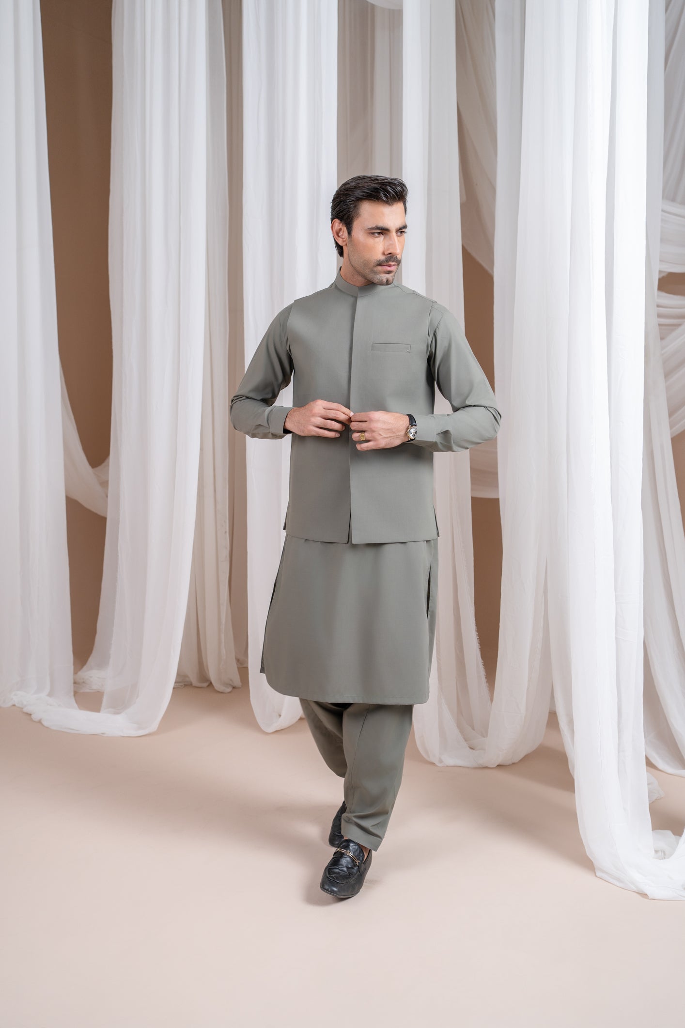A man wearing a sand grey luxury formal Kameez Shalwar with a straight cut waistcoat and a patch pocket waistcoat.