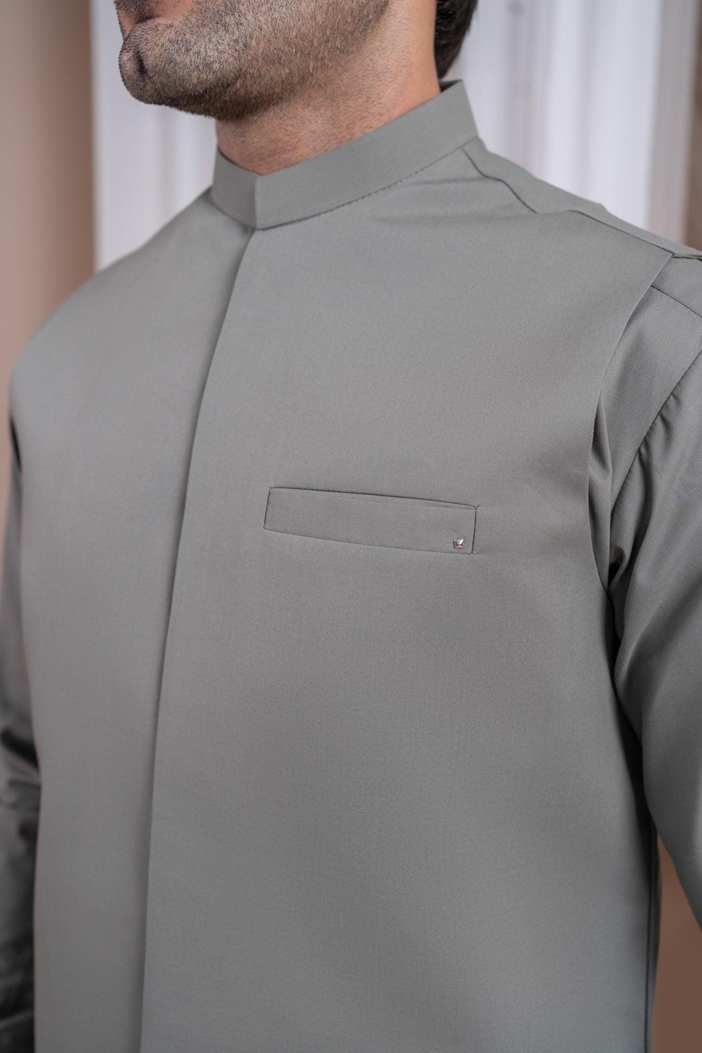 A man wearing a sand grey luxury formal Kameez Shalwar with a straight cut waistcoat and a patch pocket waistcoat.