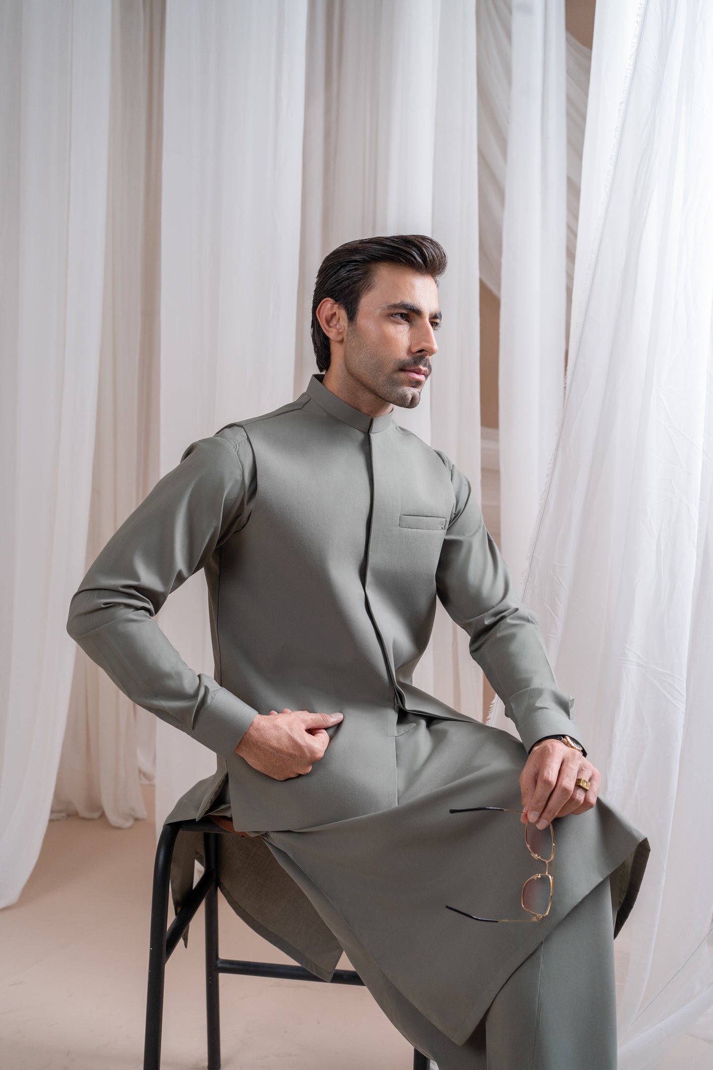 A man wearing a sand grey luxury formal Kameez Shalwar with a straight cut waistcoat and a patch pocket waistcoat.