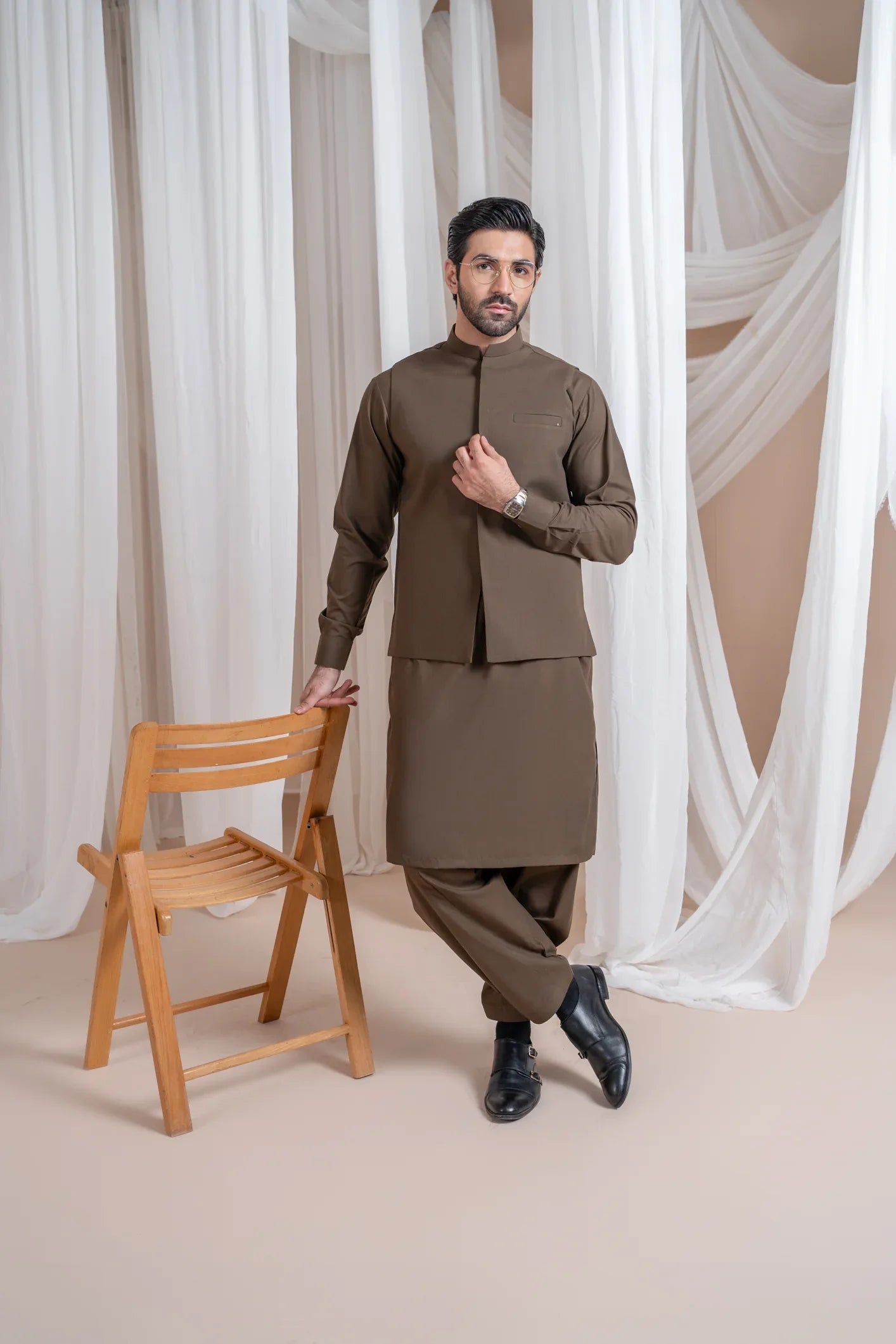 A man wearing a light brown luxury formal Kameez Shalwar with a straight cut and a patch pocket waistcoat.