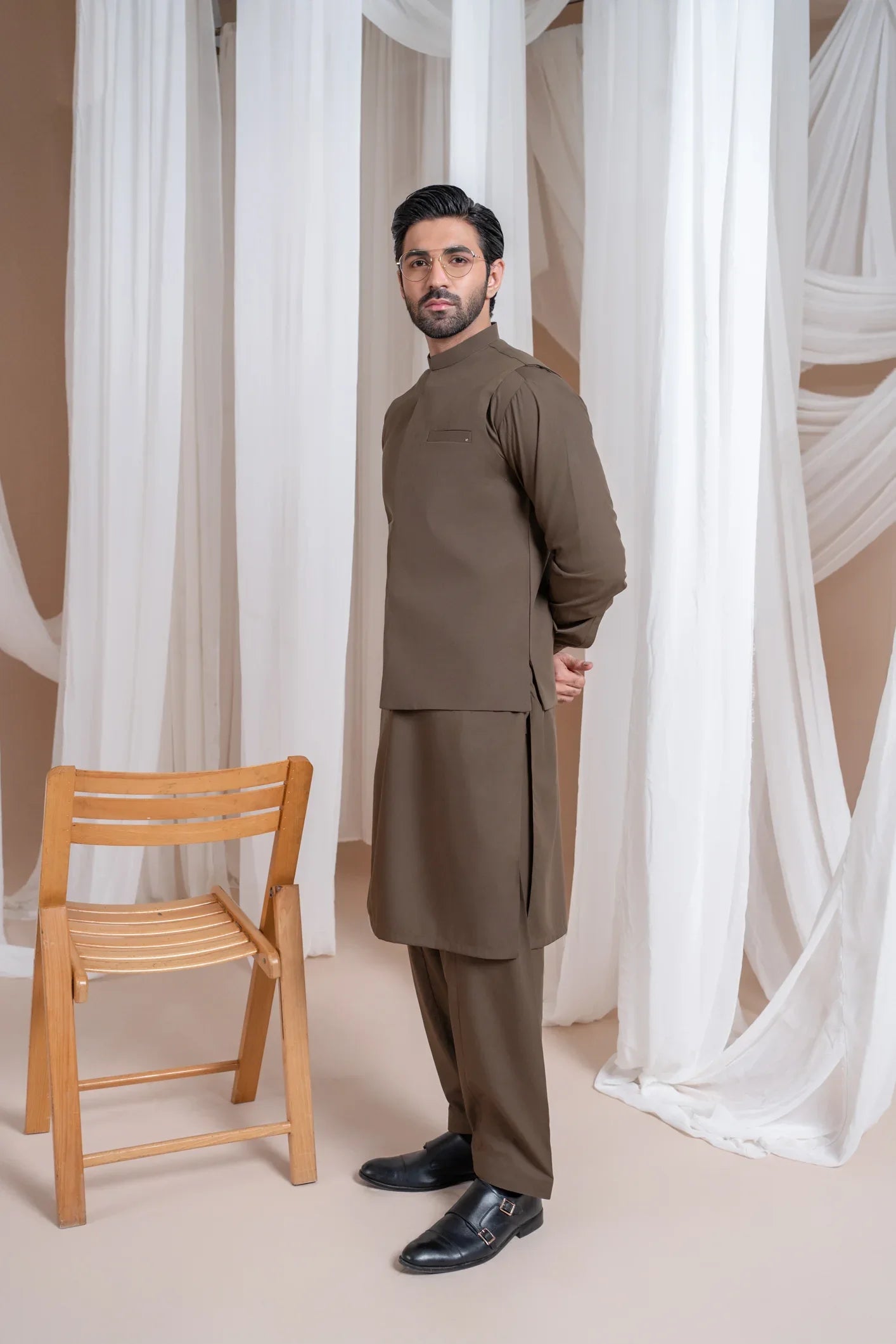 A man wearing a light brown luxury formal Kameez Shalwar with a straight cut and a patch pocket waistcoat.