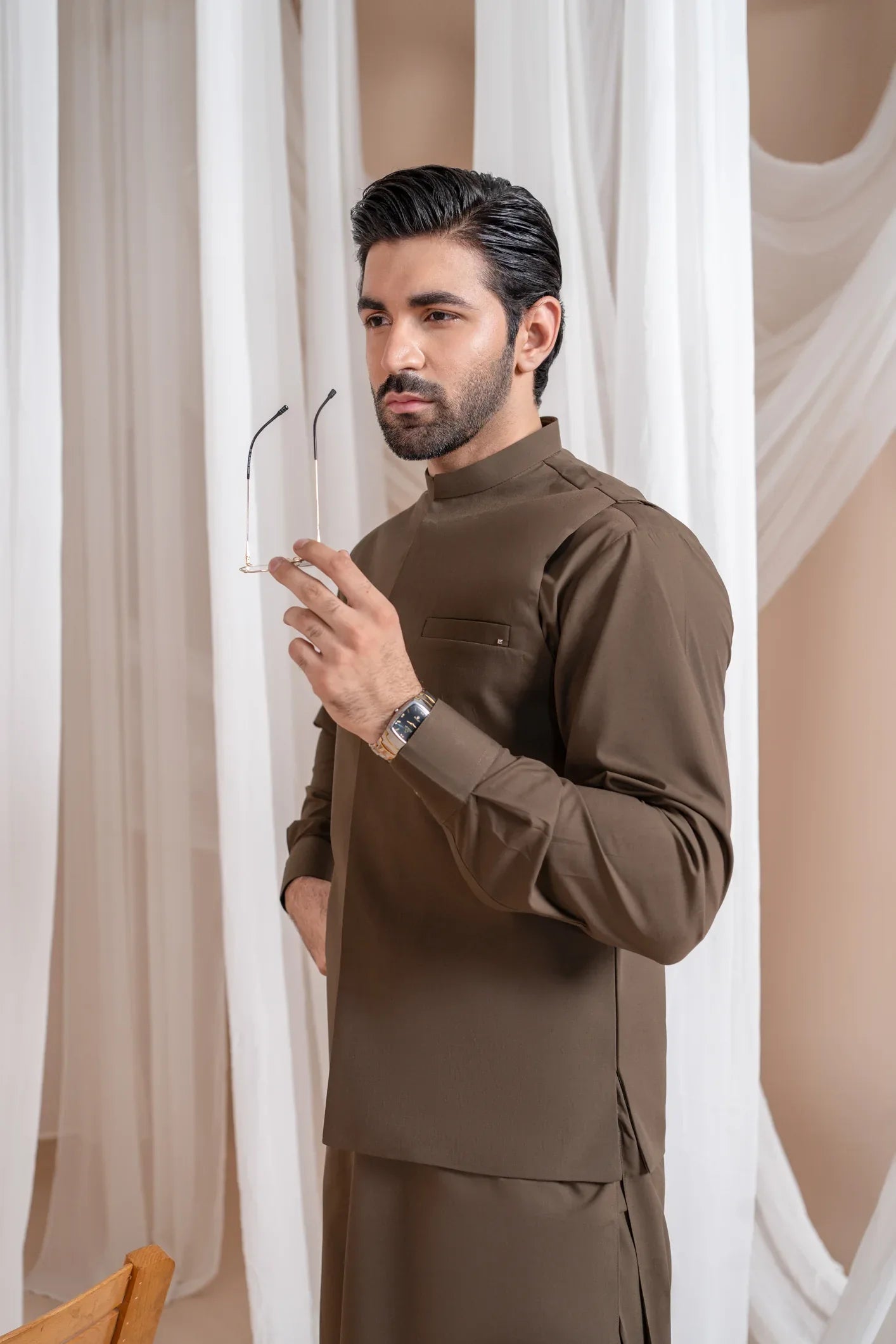 A man wearing a light brown luxury formal Kameez Shalwar with a straight cut and a patch pocket waistcoat.