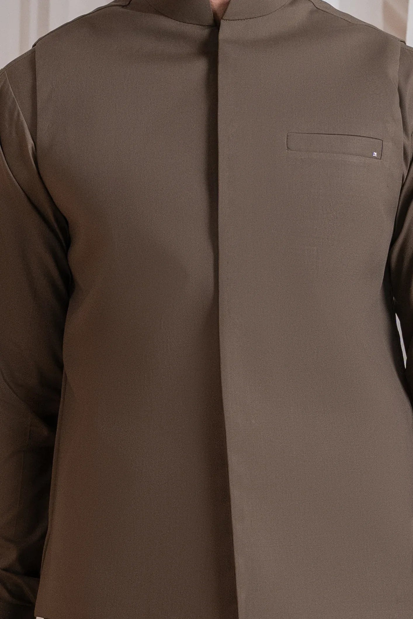 A man standing wearing a light brown straight cut luxury blended waistcoat with a mandarin collar and full sleeves.