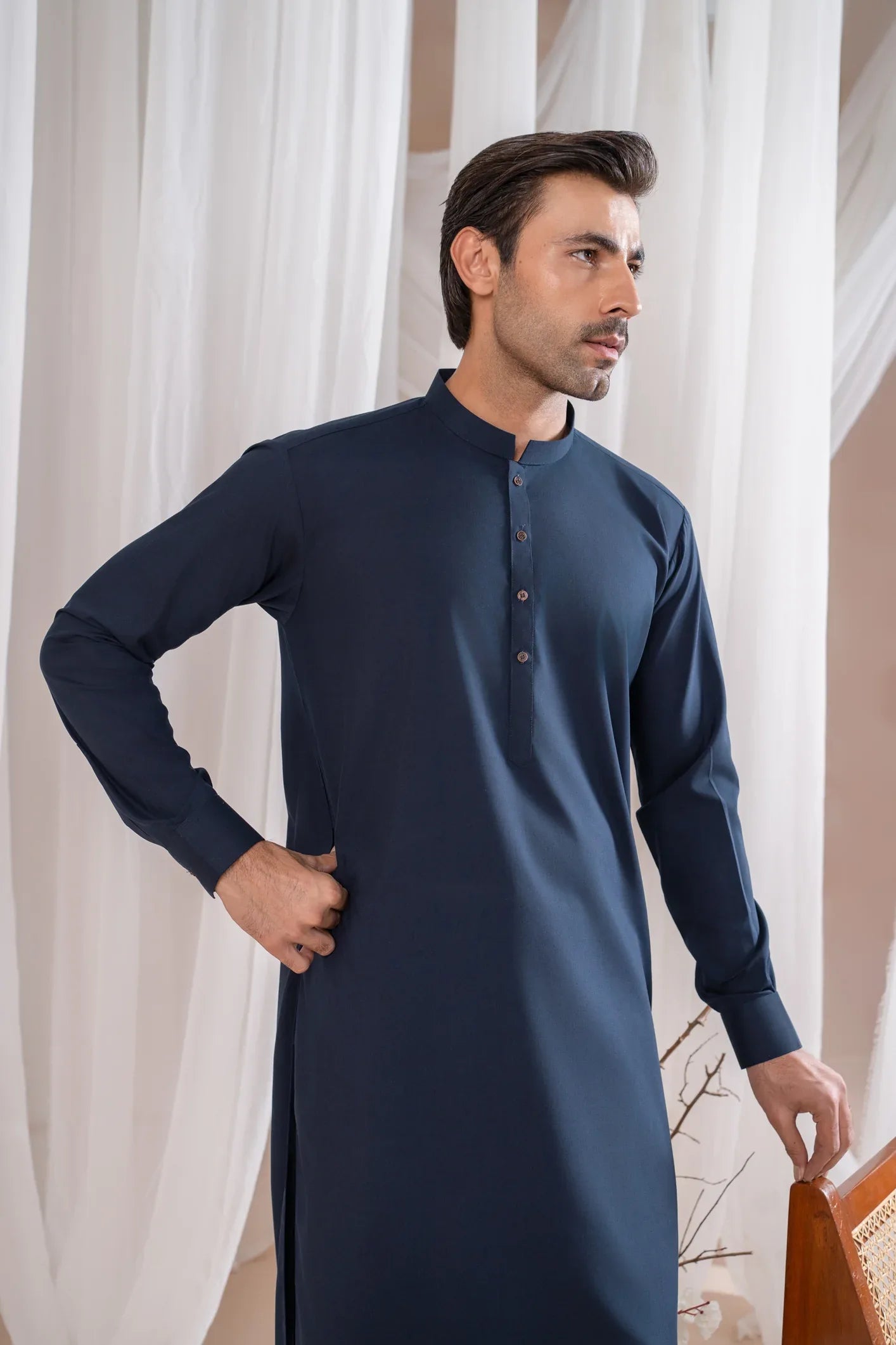 A man wearing a navy blue kameez shalwar with a mandarin collar and full sleeves.