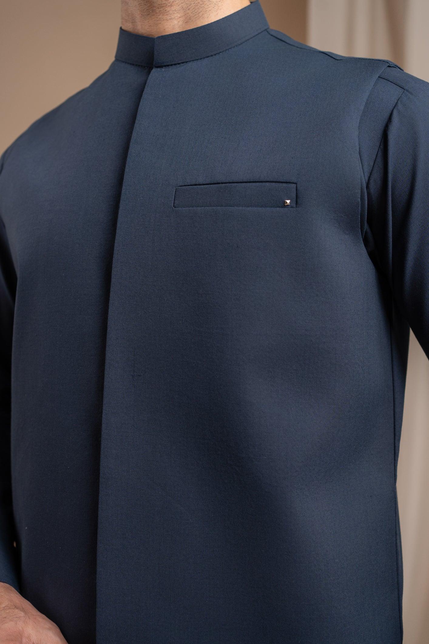 A man wearing a navy blue formal kameez shalwar with a blended waistcoat and full sleeves. He is standing against a neutral backdrop.