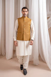 Man wearing a kameez shalwar with a camel brown waistcoat against a white curtain background