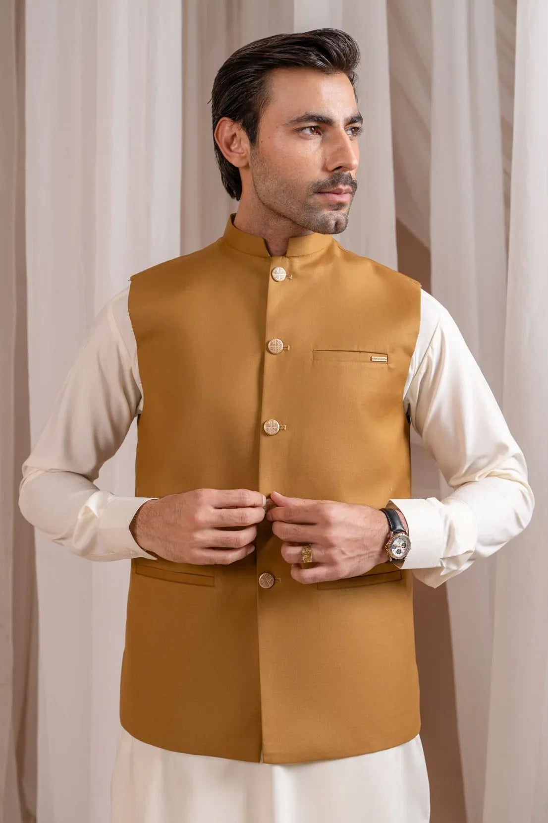 A man wearing a camel suiting waistcoat with a straight cut and classic button design over a white shirt.