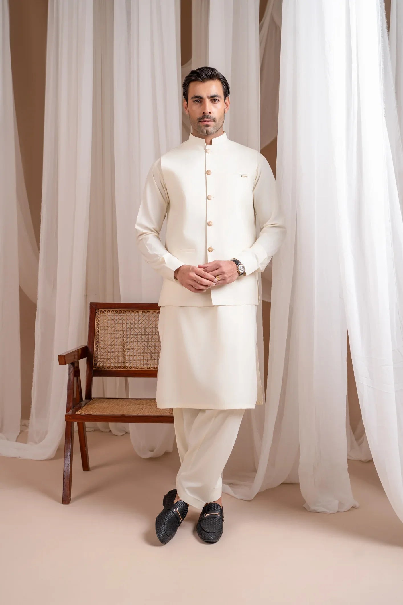 A man wearing a bosky white luxury formal kameez shalwar with a straight cut buttoned blended waistcoat.