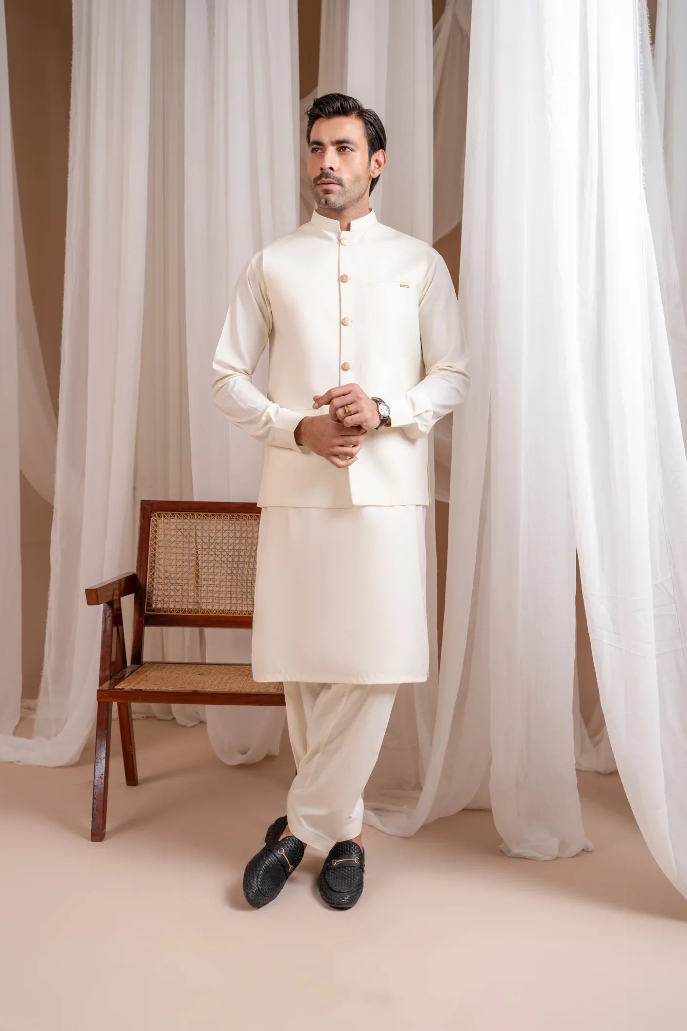 A man wearing a bosky white luxury formal kameez shalwar with a straight cut buttoned blended waistcoat.