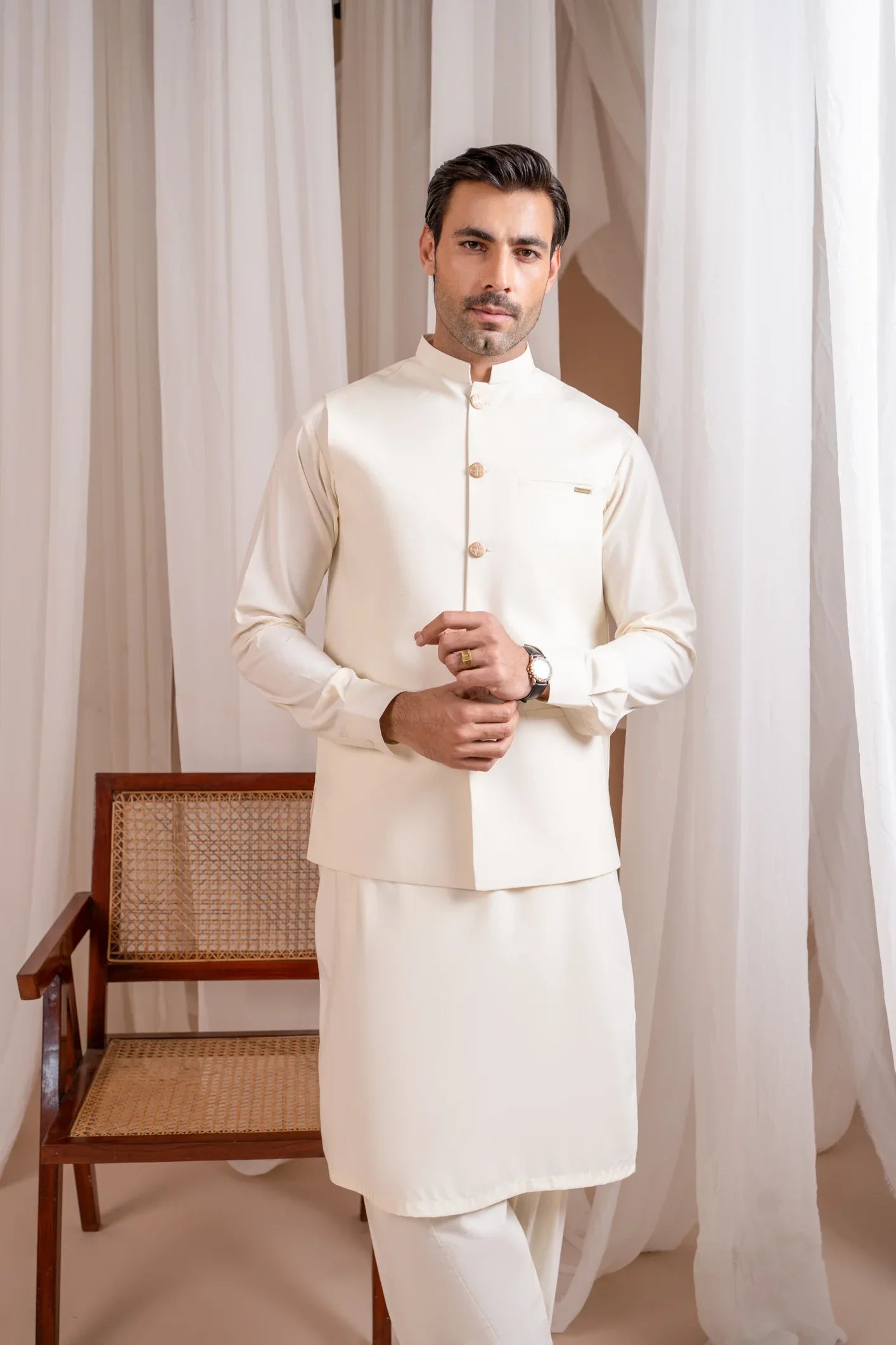A man wearing a bosky white luxury formal kameez shalwar with a straight cut buttoned blended waistcoat.