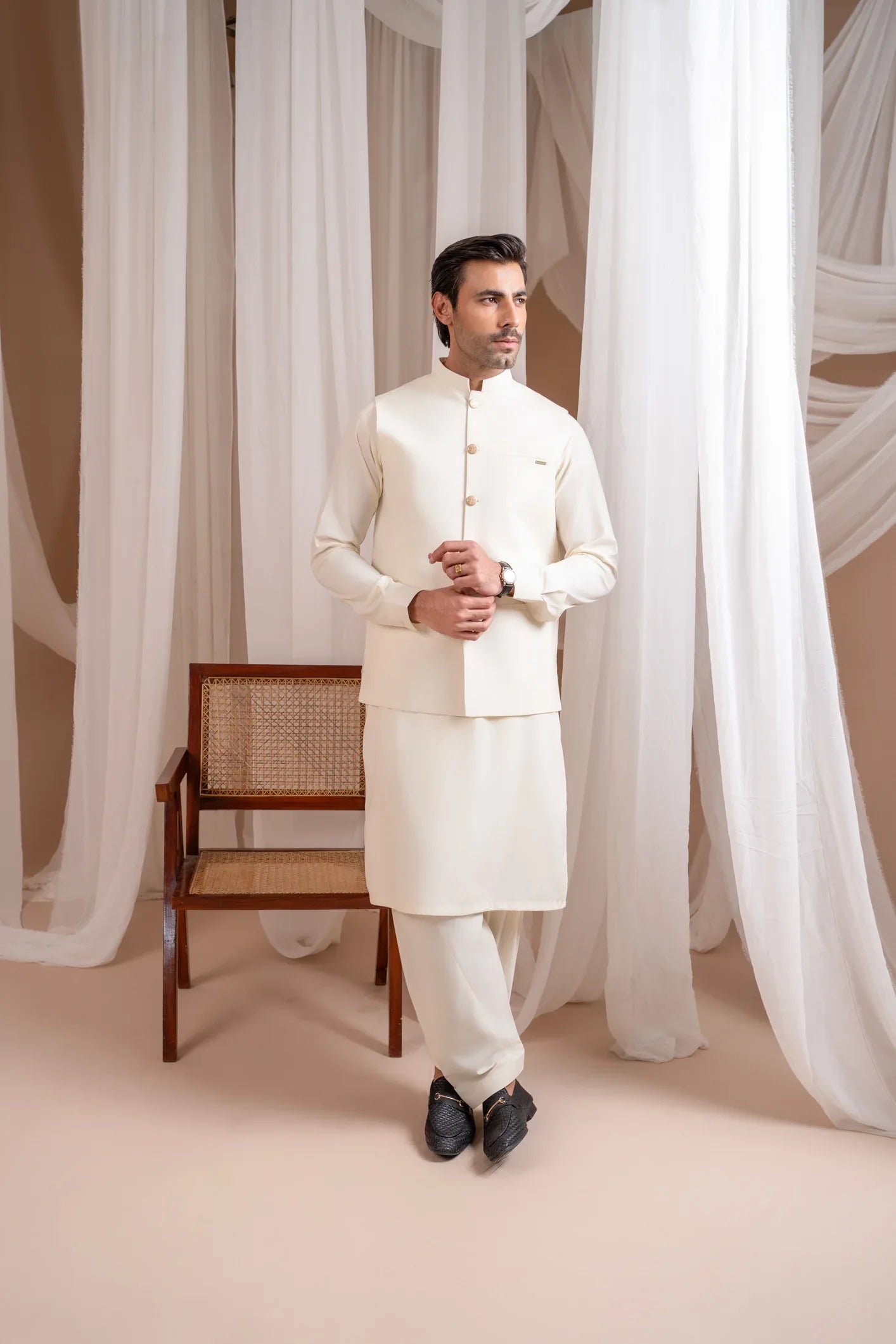 A man wearing a bosky white luxury formal kameez shalwar with a straight cut buttoned blended waistcoat.