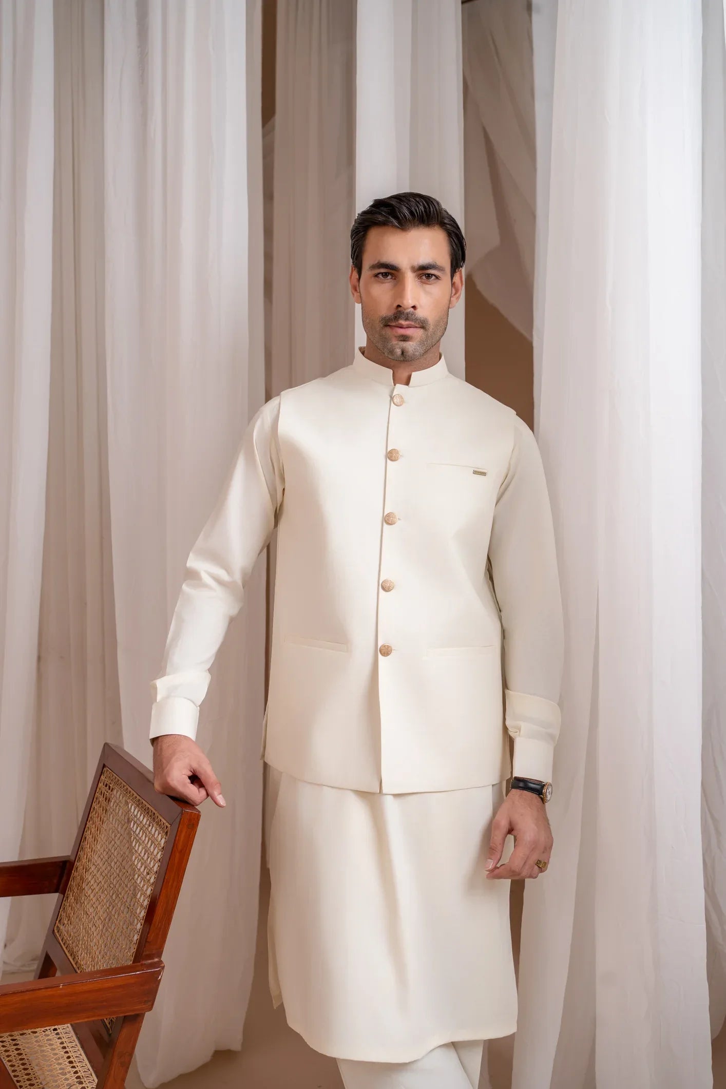 A man wearing a Bosky White luxury blended waistcoat with a mandarin collar and straight cut buttoned design, paired with kameez shalwar and trousers.