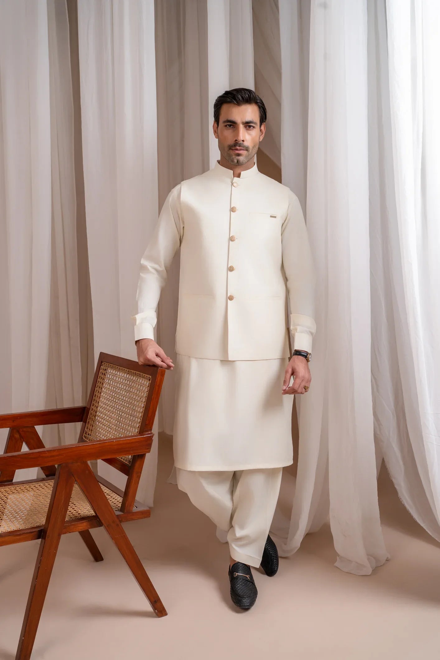 A man wearing a bosky white luxury formal kameez shalwar with a straight cut buttoned blended waistcoat.