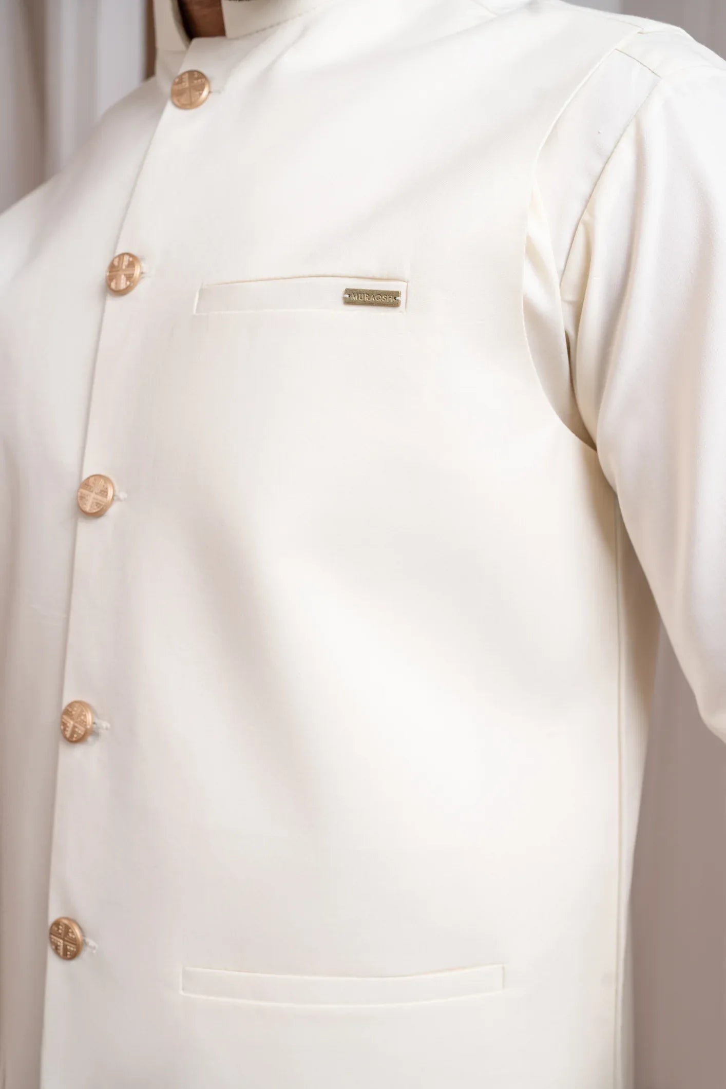 A man wearing a bosky white luxury formal kameez shalwar with a straight cut buttoned blended waistcoat.