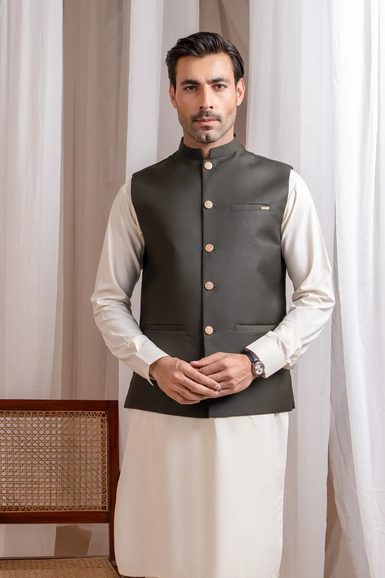 Man wearing a army green suiting waistcoat over bosky white kameez shalwar with a neutral background
