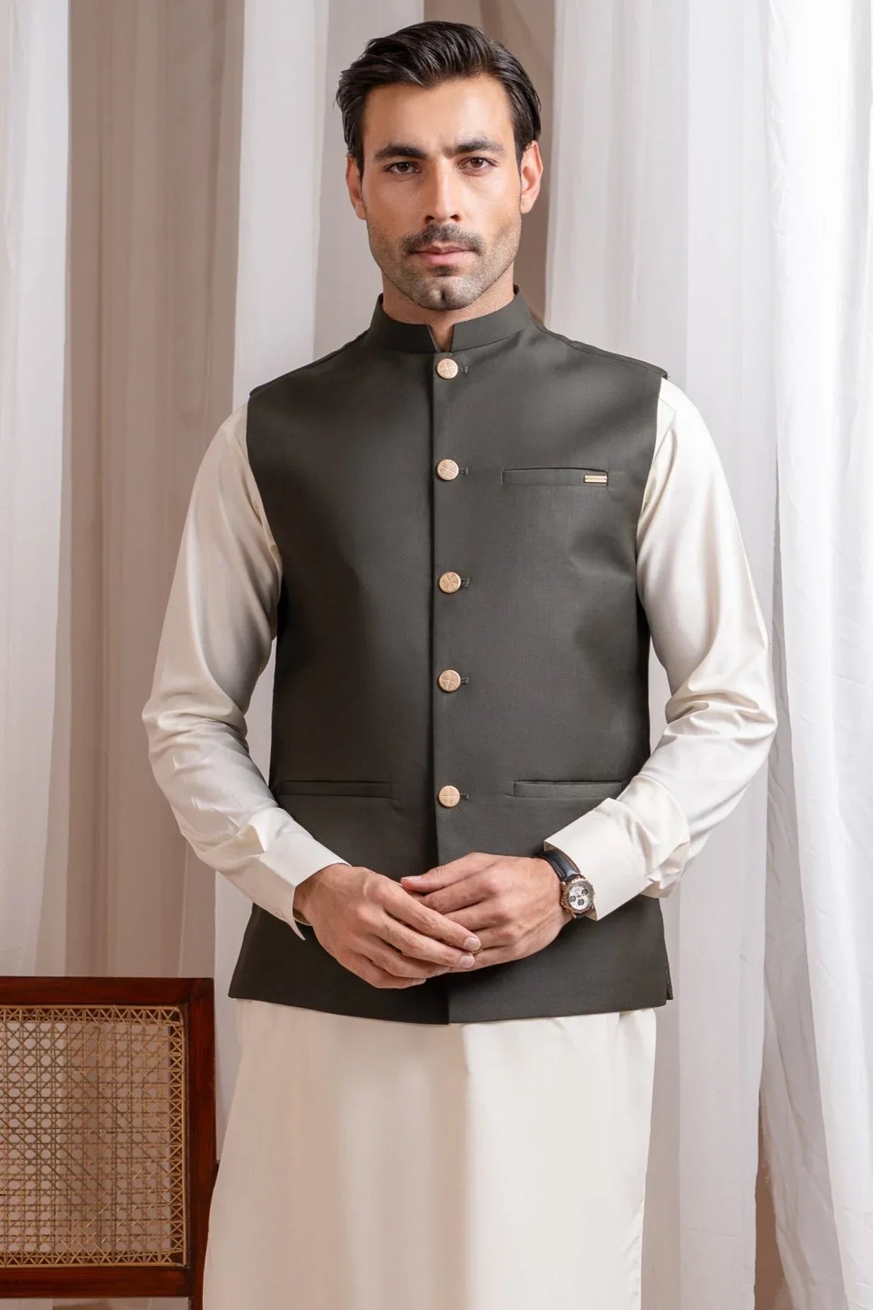 A man wearing am army green suiting waistcoat with a straight cut and classic buttons over a white shirt.