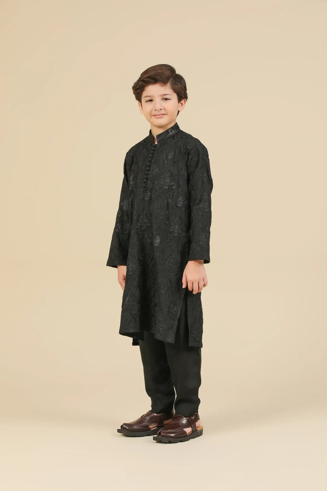Young boy wearing a black raw silk embroidered kurta trouser outfit on a beige background