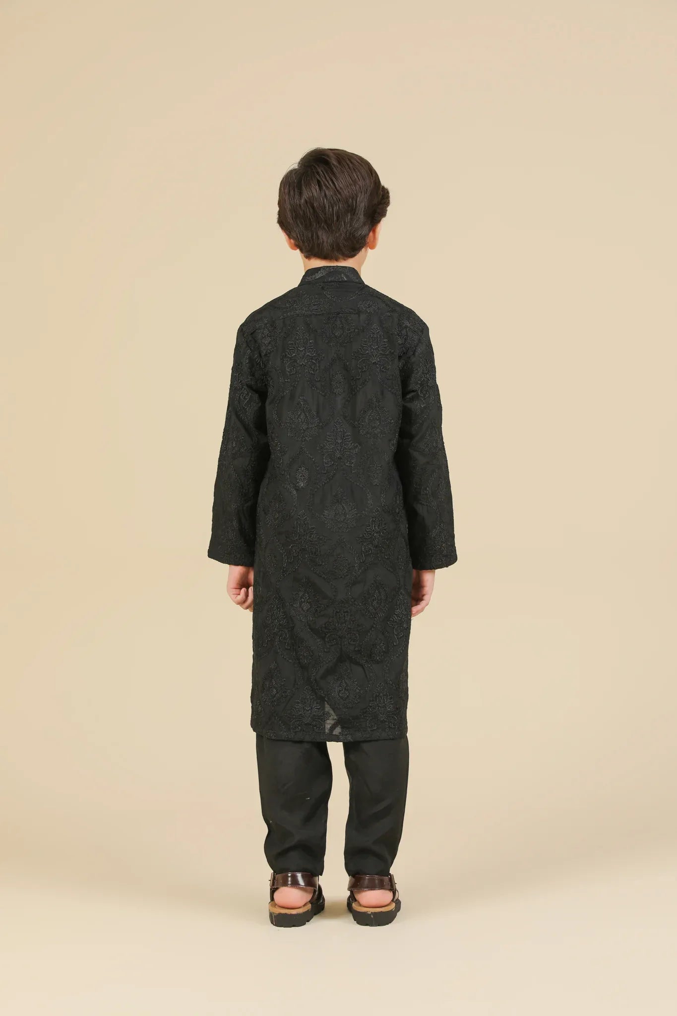Young boy wearing a black raw silk embroidered kurta trouser outfit on a beige background