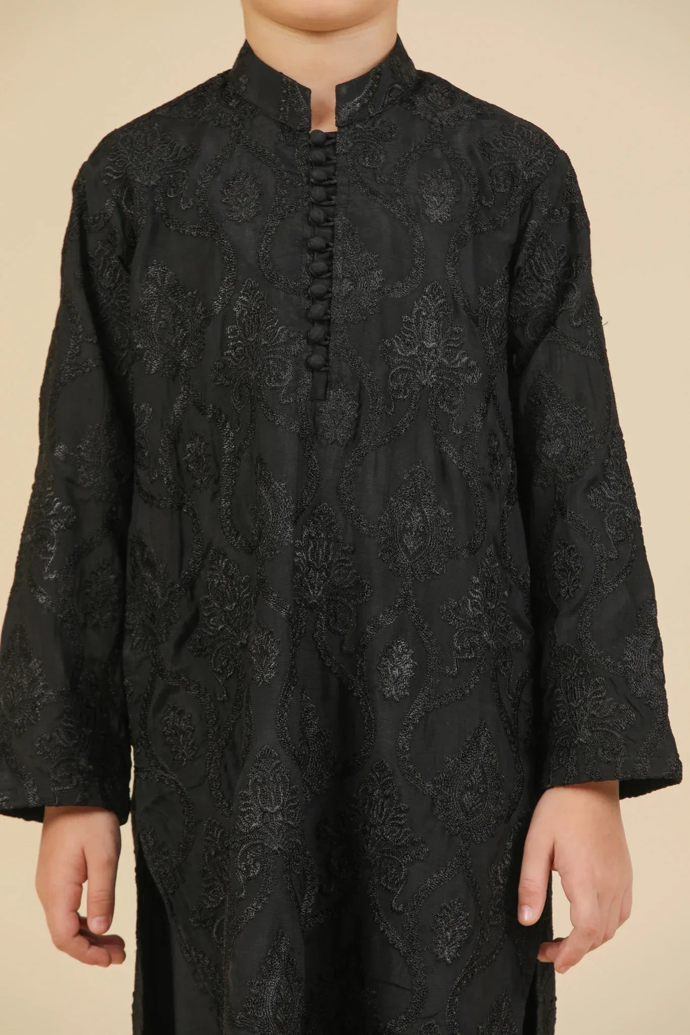 Young boy wearing a black raw silk embroidered kurta trouser outfit on a beige background
