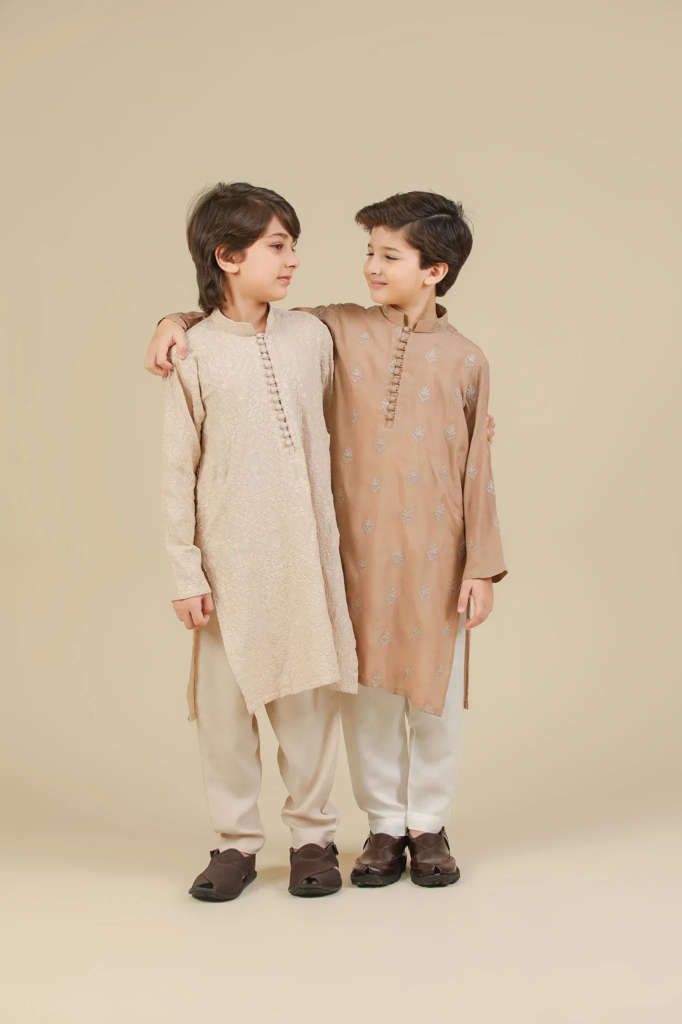 Children wearing a beige raw silk embroidered kurta trouser and peach raw silk embroidered kurta pajama on a beige background
