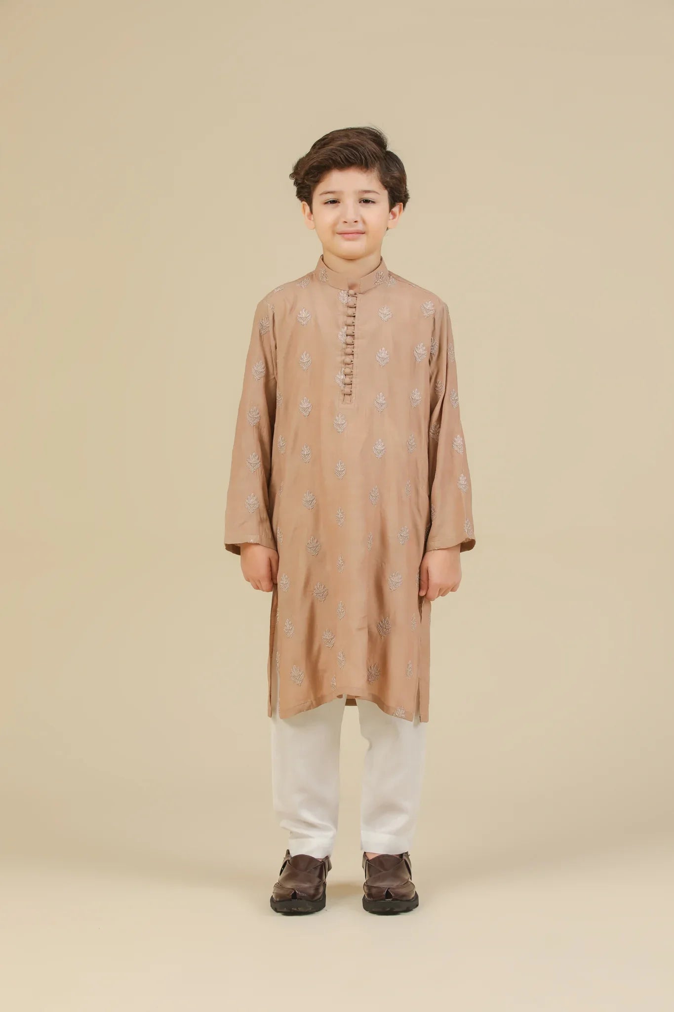Young boy wearing a peach raw silk embroidered kurta with white trouser on a beige background