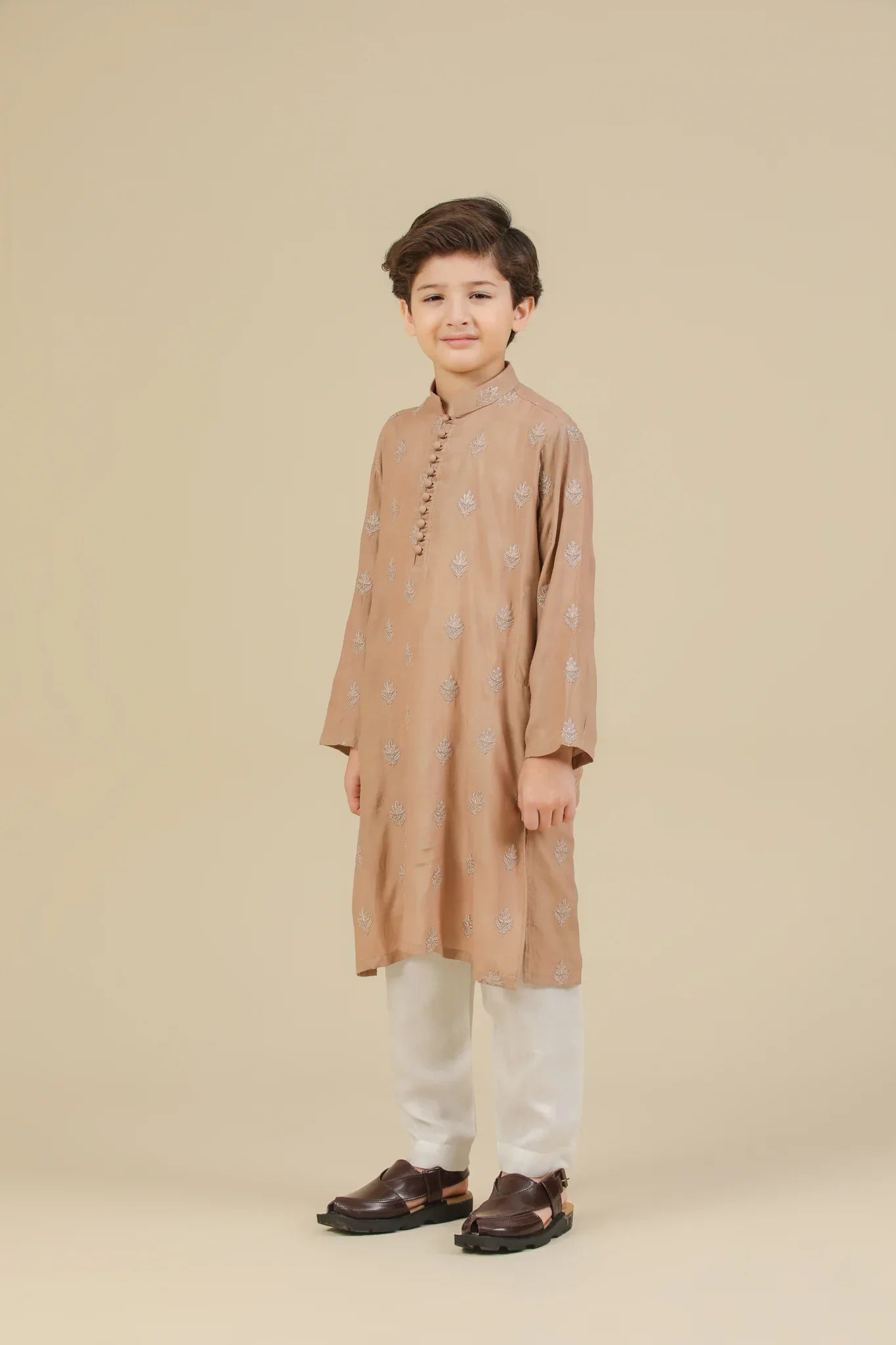 Young boy wearing a peach raw silk embroidered kurta with white trouser on a beige background
