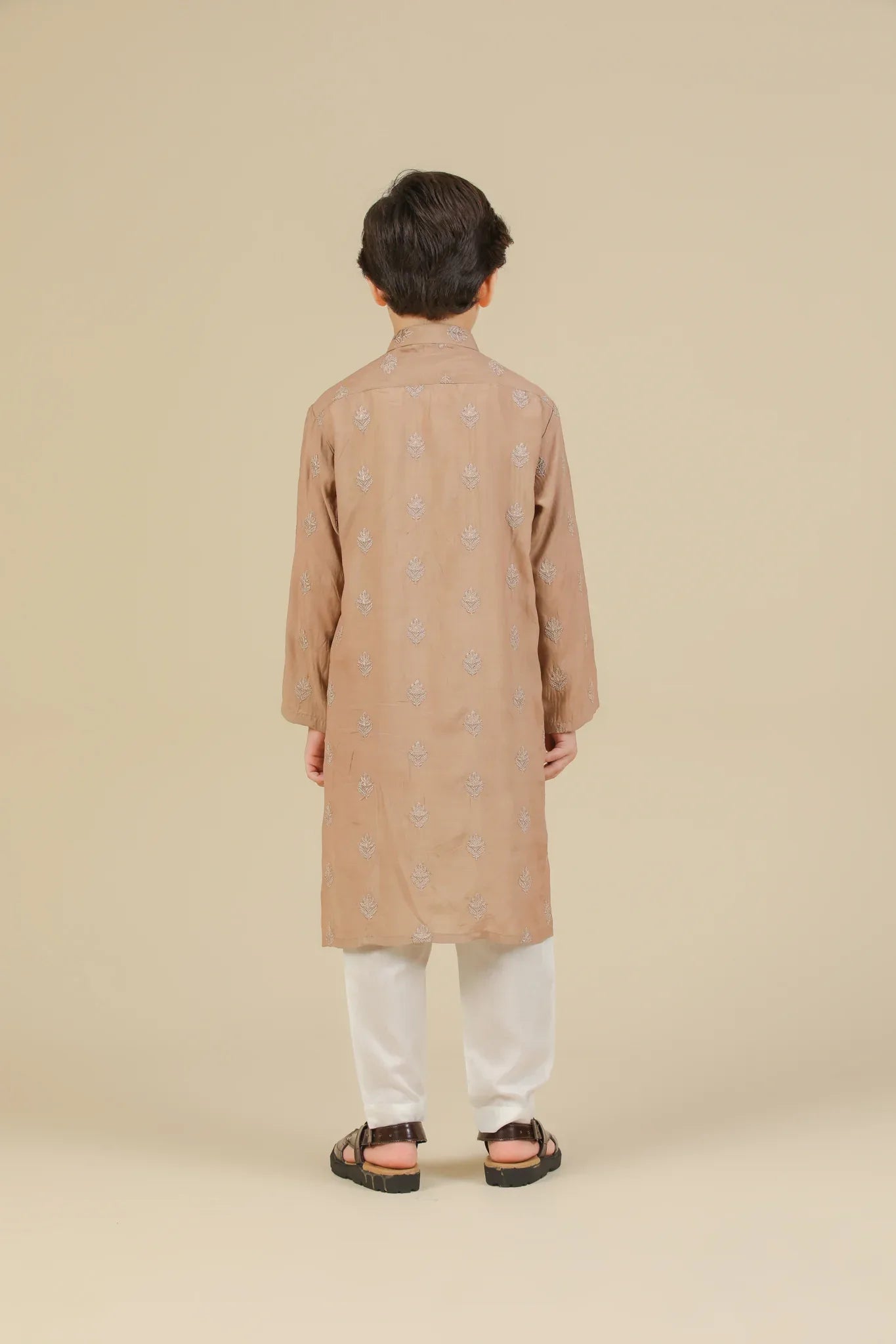 Young boy wearing a peach raw silk embroidered kurta with white trouser on a beige background