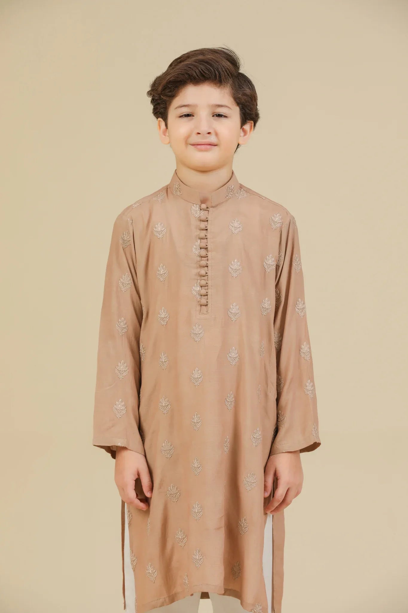 Young boy wearing a peach raw silk embroidered kurta with white trouser on a beige background