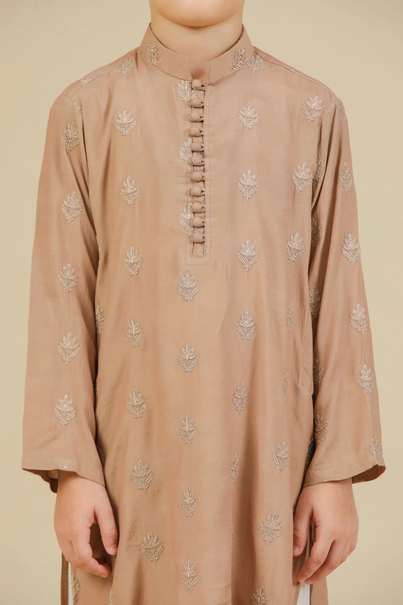 Young boy wearing a peach raw silk embroidered kurta with white trouser on a beige background