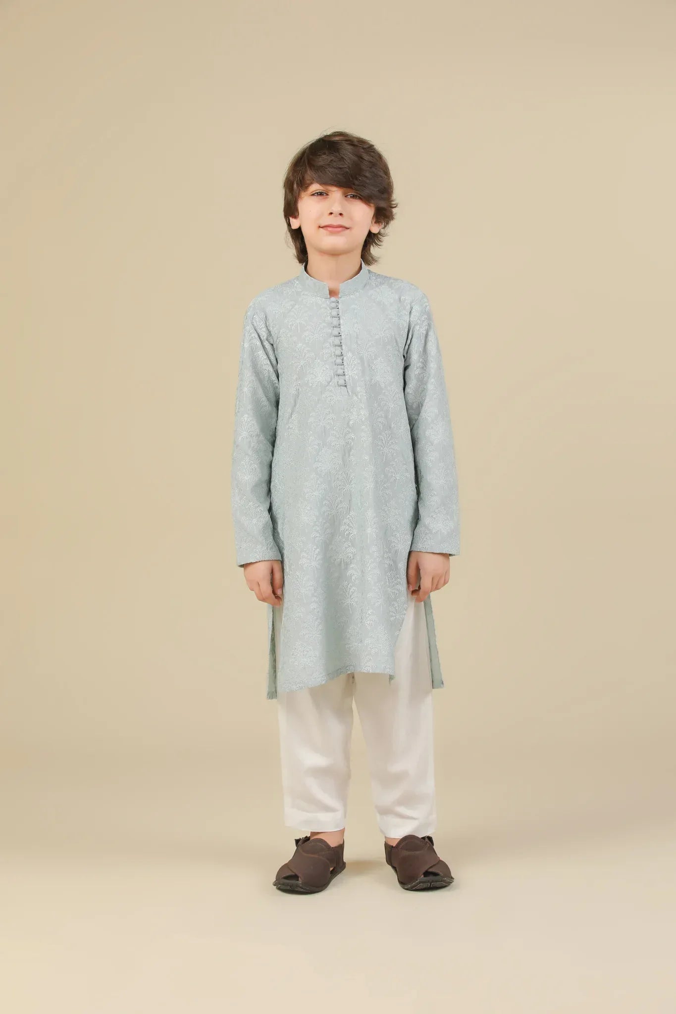 Young boy wearing an ice blue embroidered kurta with white pajama on a beige background