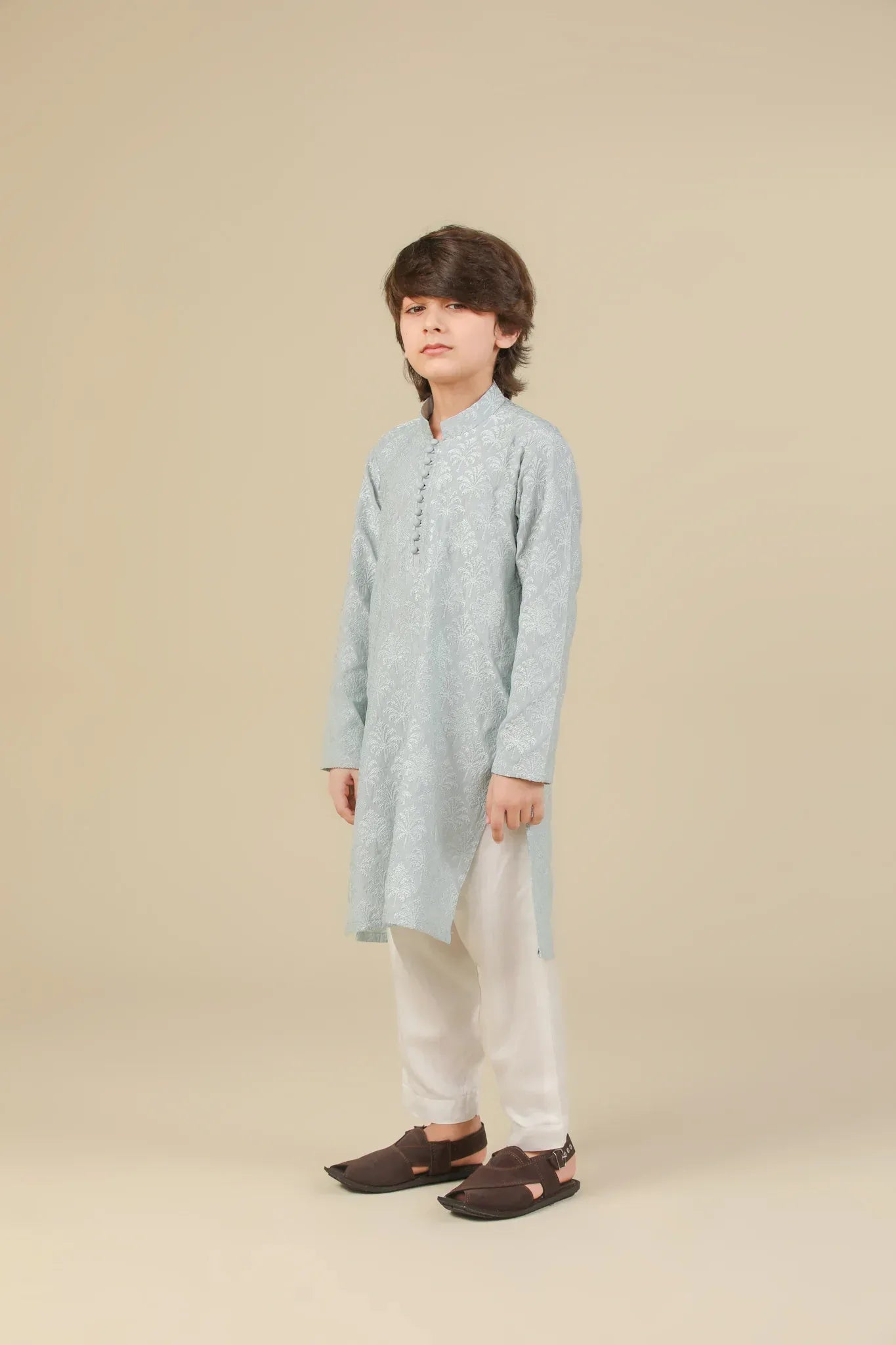Young boy wearing an ice blue embroidered kurta with white pajama on a beige background