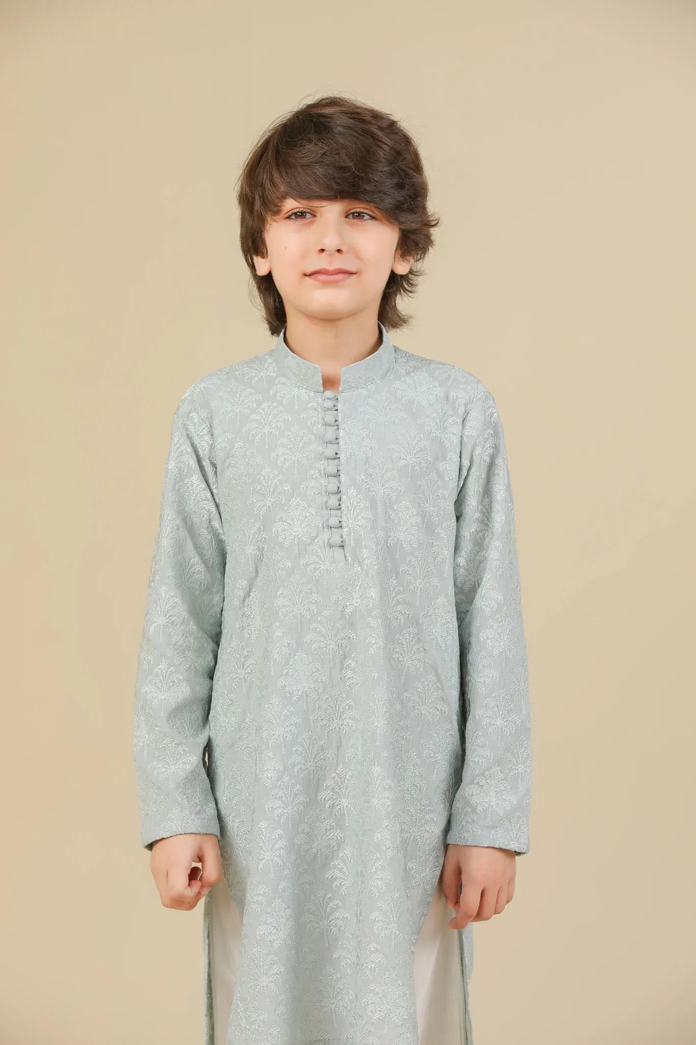 Young boy wearing an ice blue embroidered kurta with white pajama on a beige background