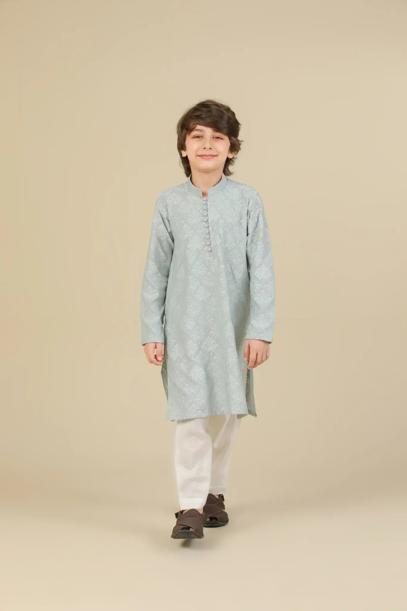 Young boy wearing an ice blue embroidered kurta with white pajama on a beige background