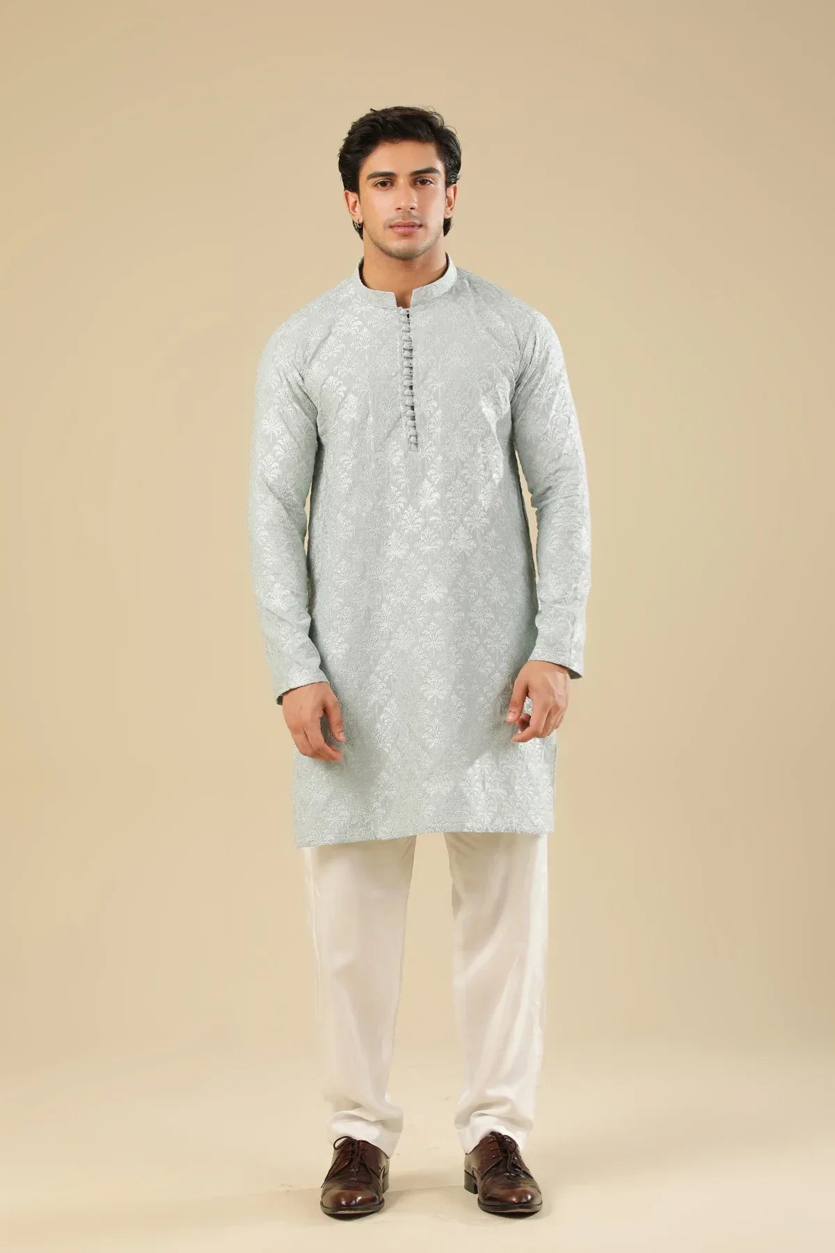 Man wearing a ice blue raw silk embroidered kurta trouser against a beige background