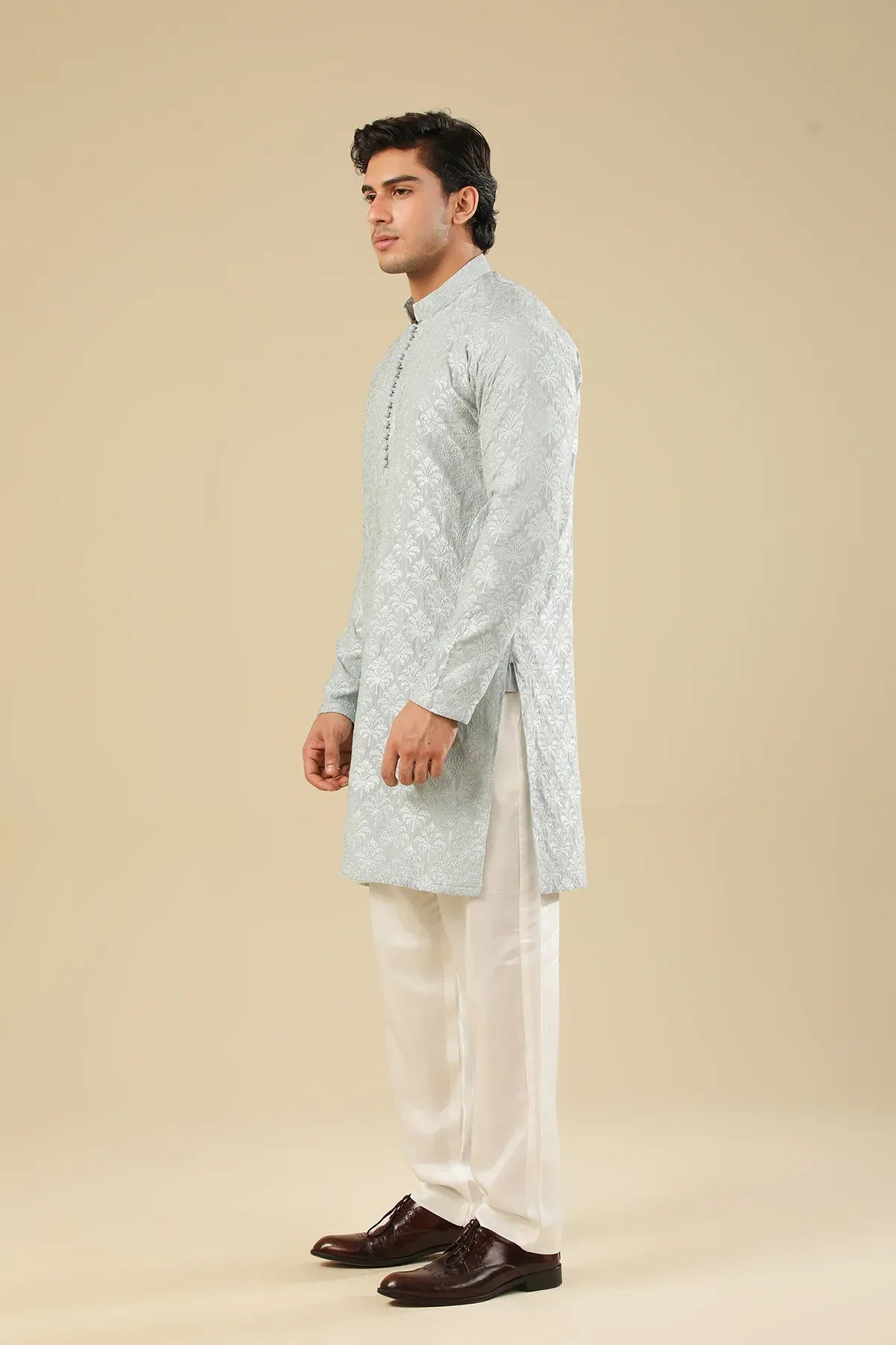 Man wearing a ice blue raw silk embroidered kurta trouser against a beige background
