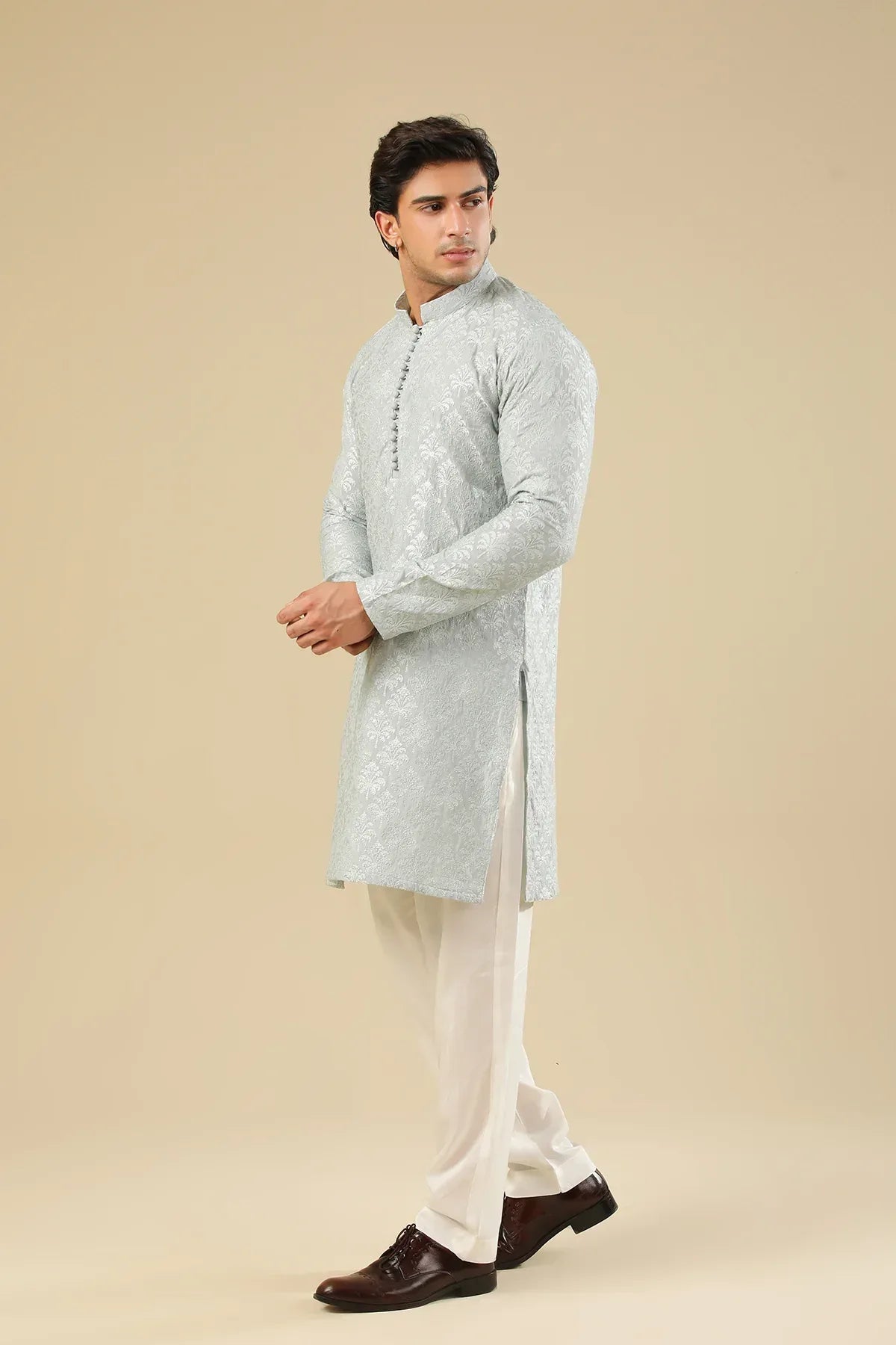Man wearing a ice blue raw silk embroidered kurta trouser against a beige background
