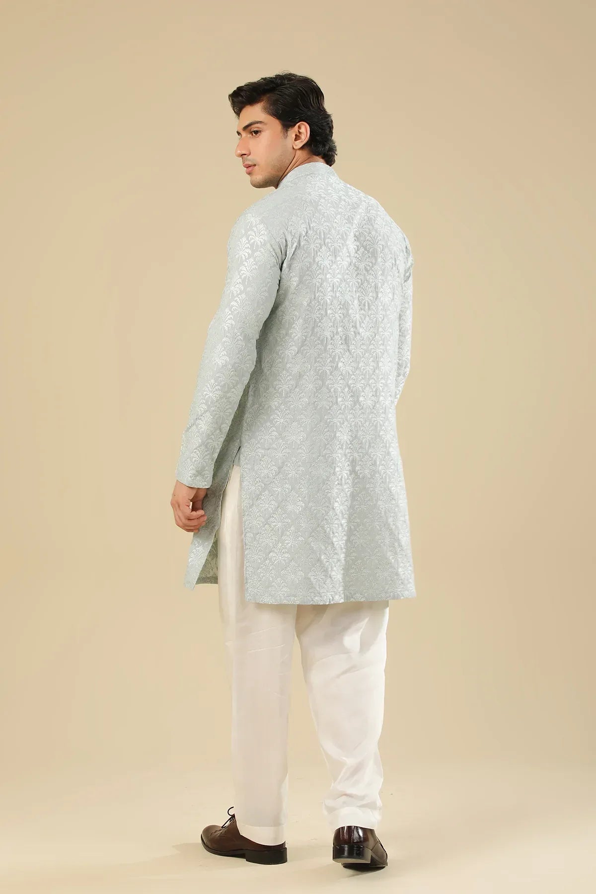 Man wearing a ice blue raw silk embroidered kurta trouser against a beige background