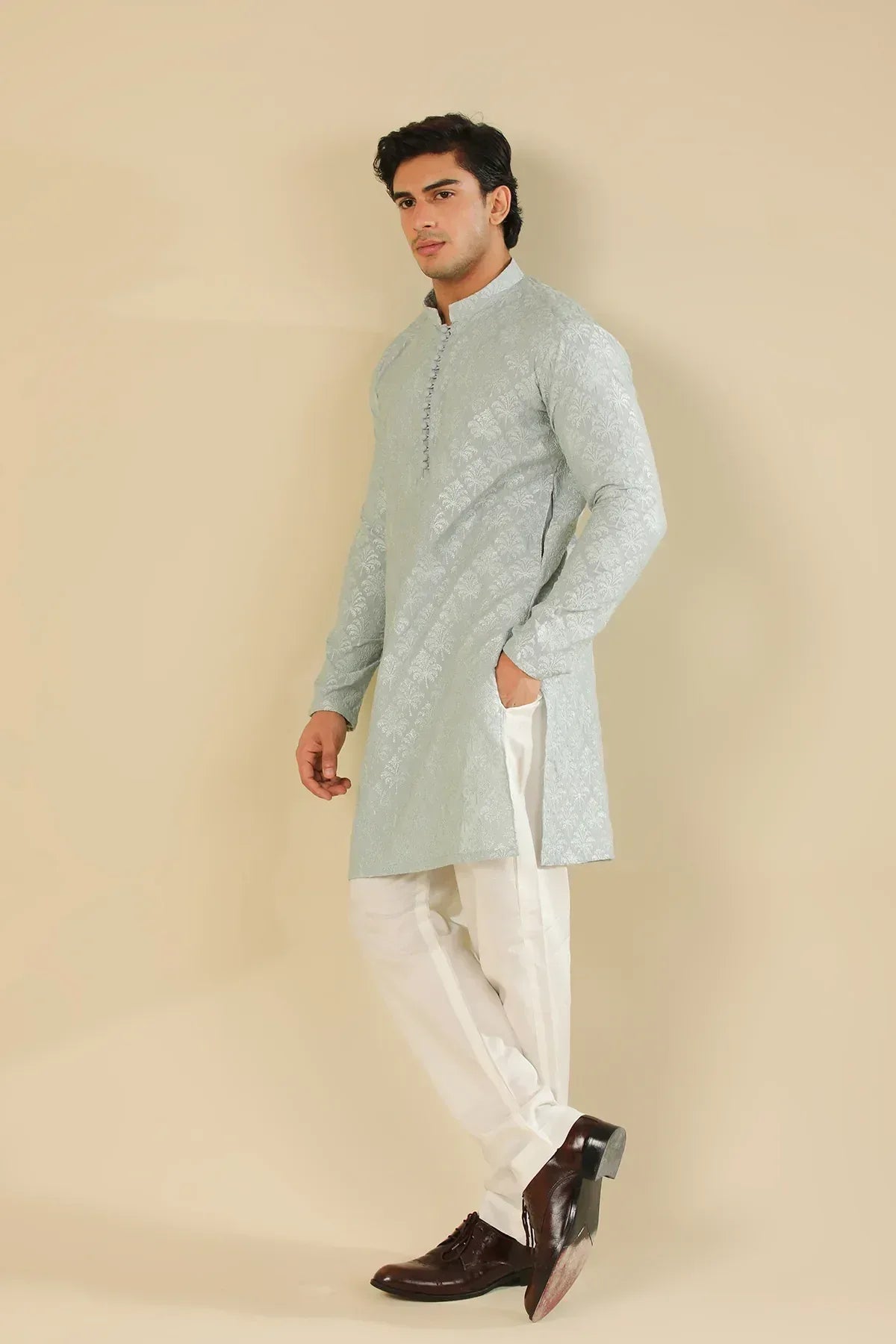 Man wearing a ice blue raw silk embroidered kurta trouser against a beige background