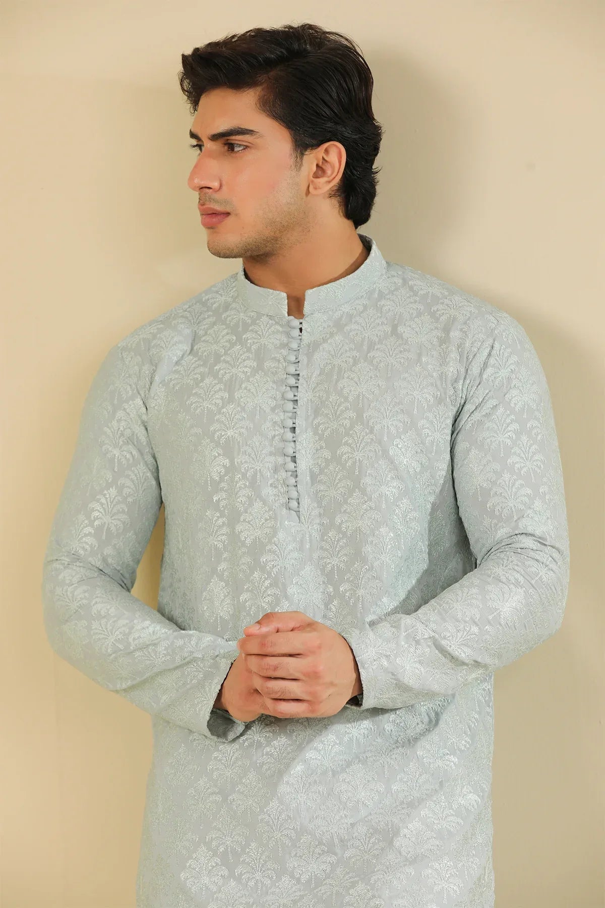 Man wearing a ice blue raw silk embroidered kurta trouser against a beige background