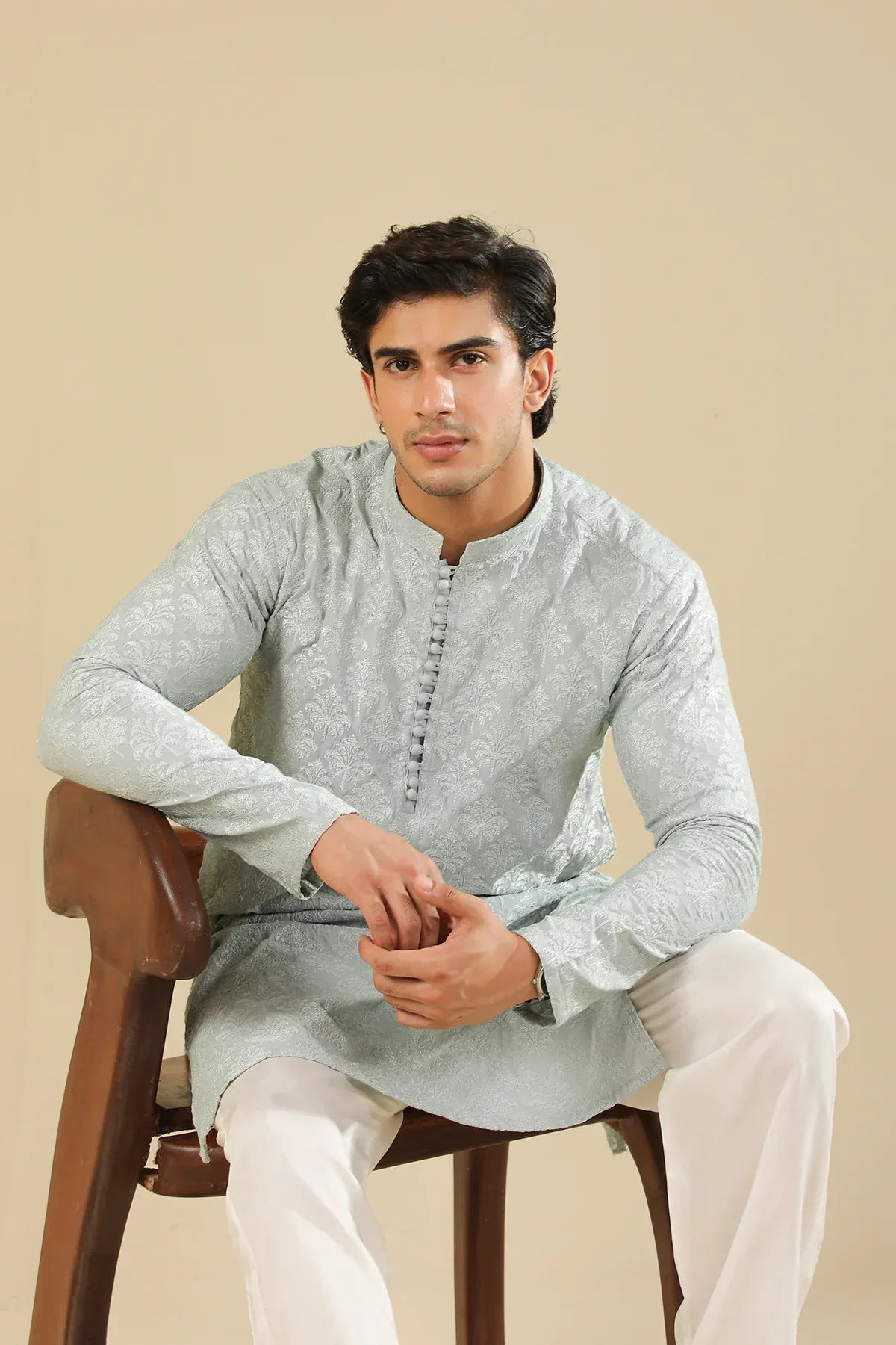 Man wearing a ice blue raw silk embroidered kurta trouser against a beige background