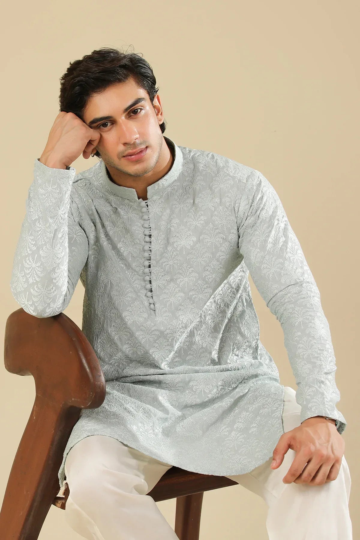 Man wearing a ice blue raw silk embroidered kurta trouser against a beige background