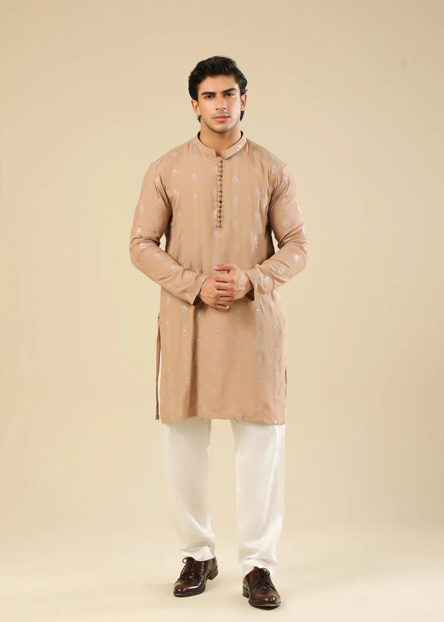 Man wearing a peach embroidered kurta and white trouser with a beige background