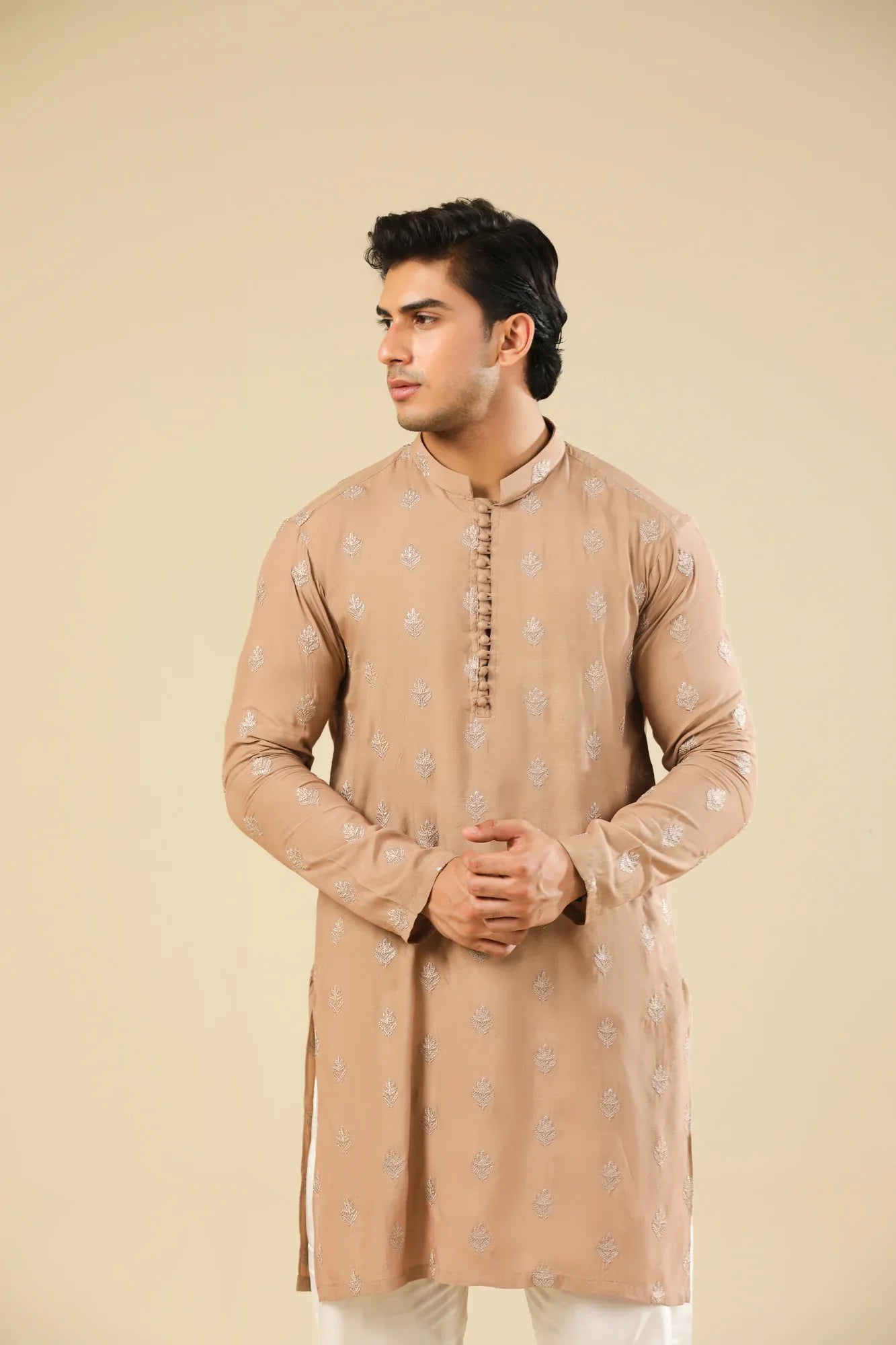 Man wearing a peach embroidered kurta and white trouser with a beige background