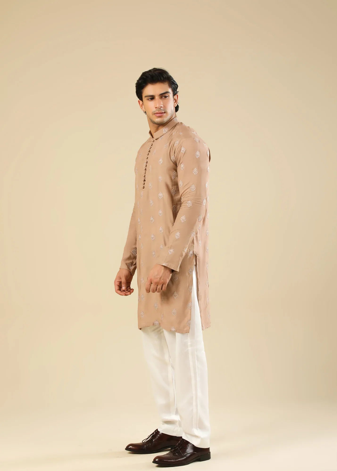 Man wearing a peach embroidered kurta and white trouser with a beige background