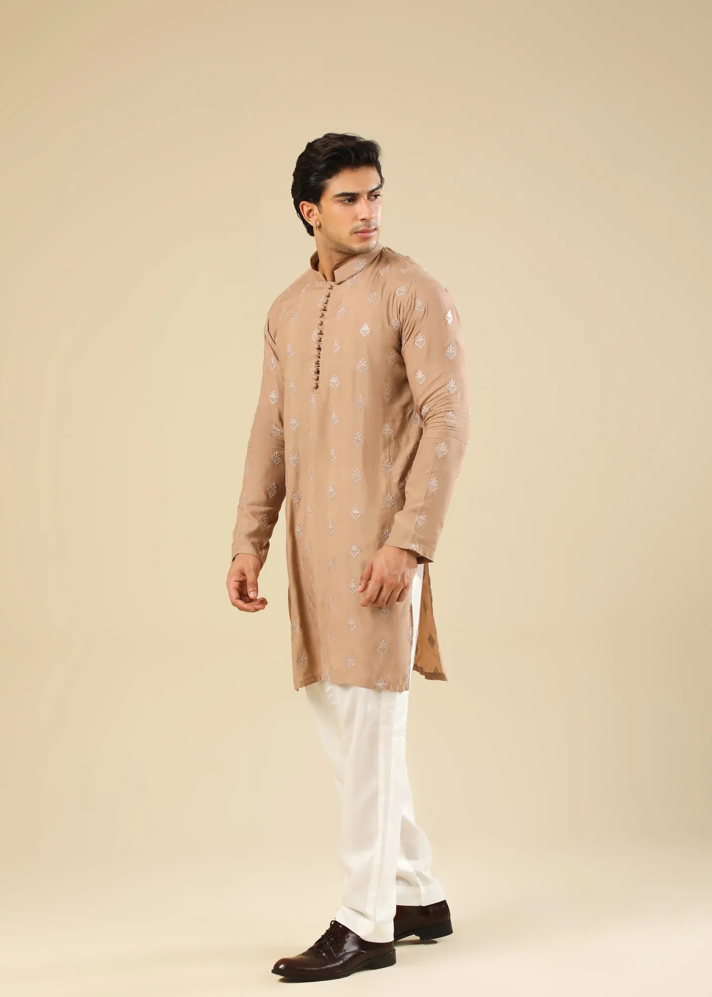 Man wearing a peach embroidered kurta and white trouser with a beige background