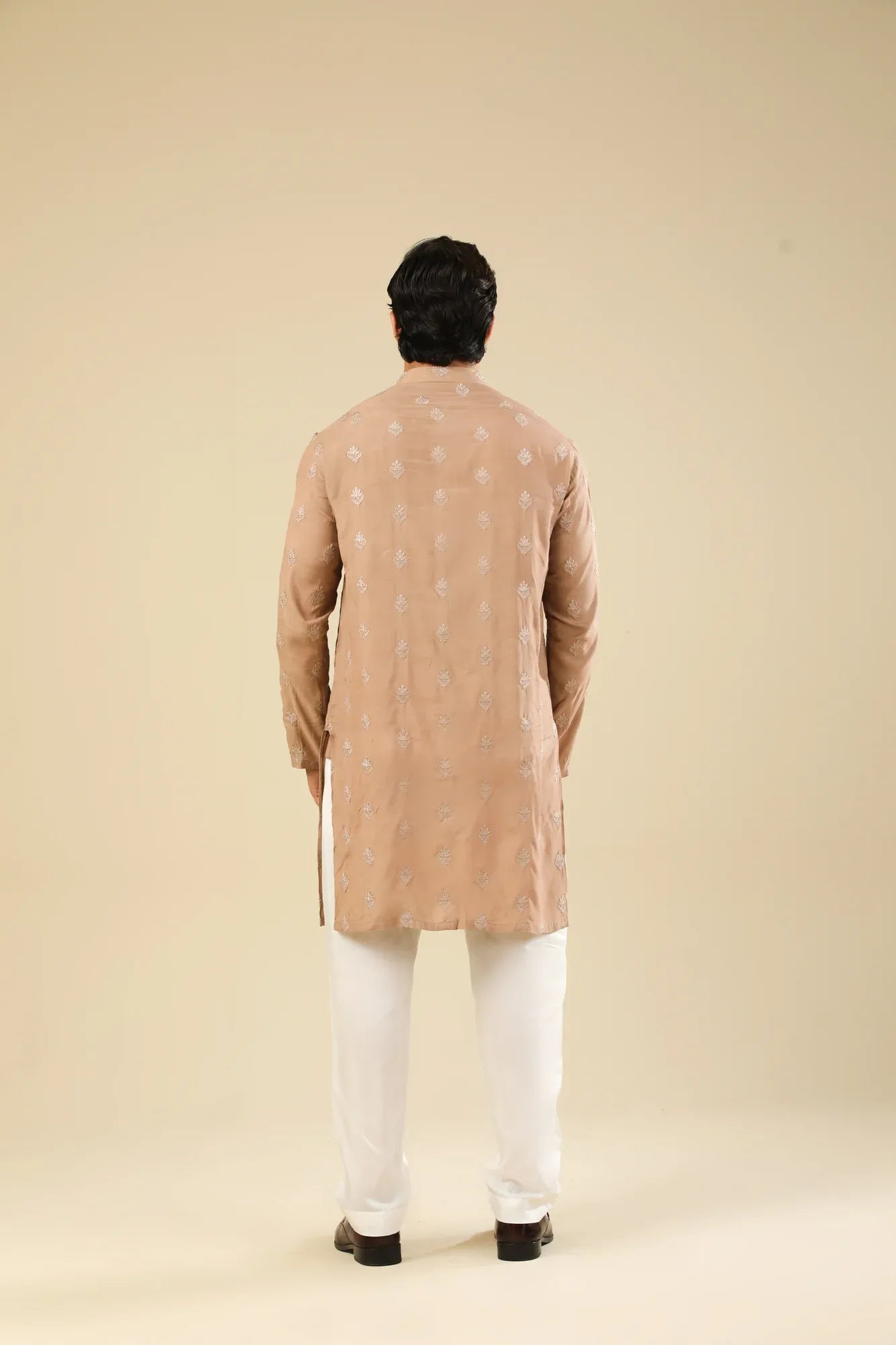 Man wearing a peach embroidered kurta and white trouser with a beige background