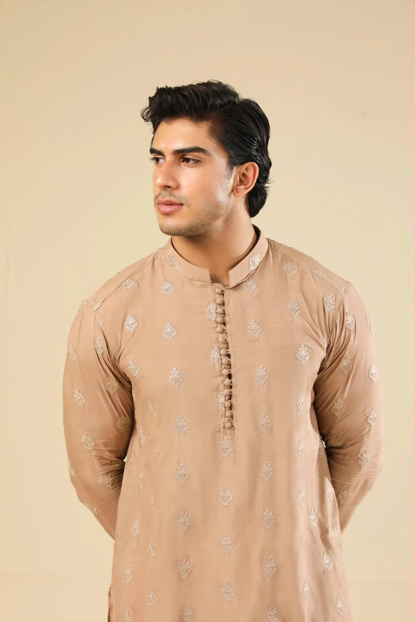 Man wearing a peach embroidered kurta and white trouser with a beige background